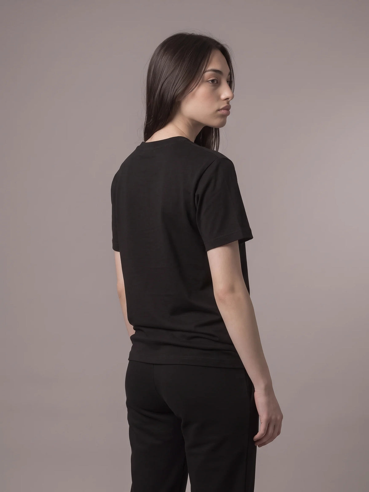 Black long fit t-shirt in organic cotton, Unidentity Core Tee, back view worn by woman looking over her shoulder, 210gsm #color_black