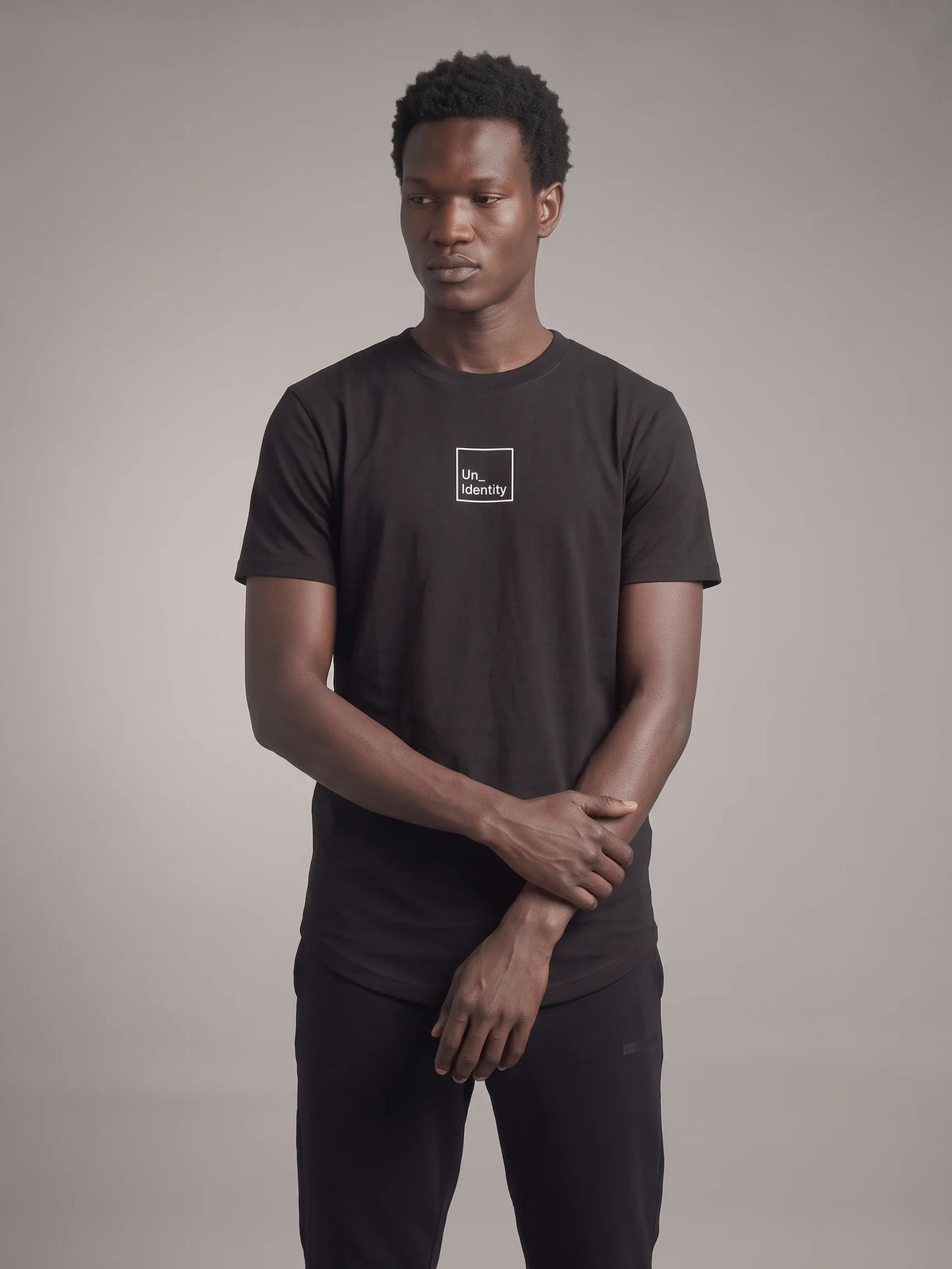 Black long fit t-shirt, Unidentity Core Long Fit Tee, front view on man showing the minimal square logo and long curved hem, organic cotton #color_black