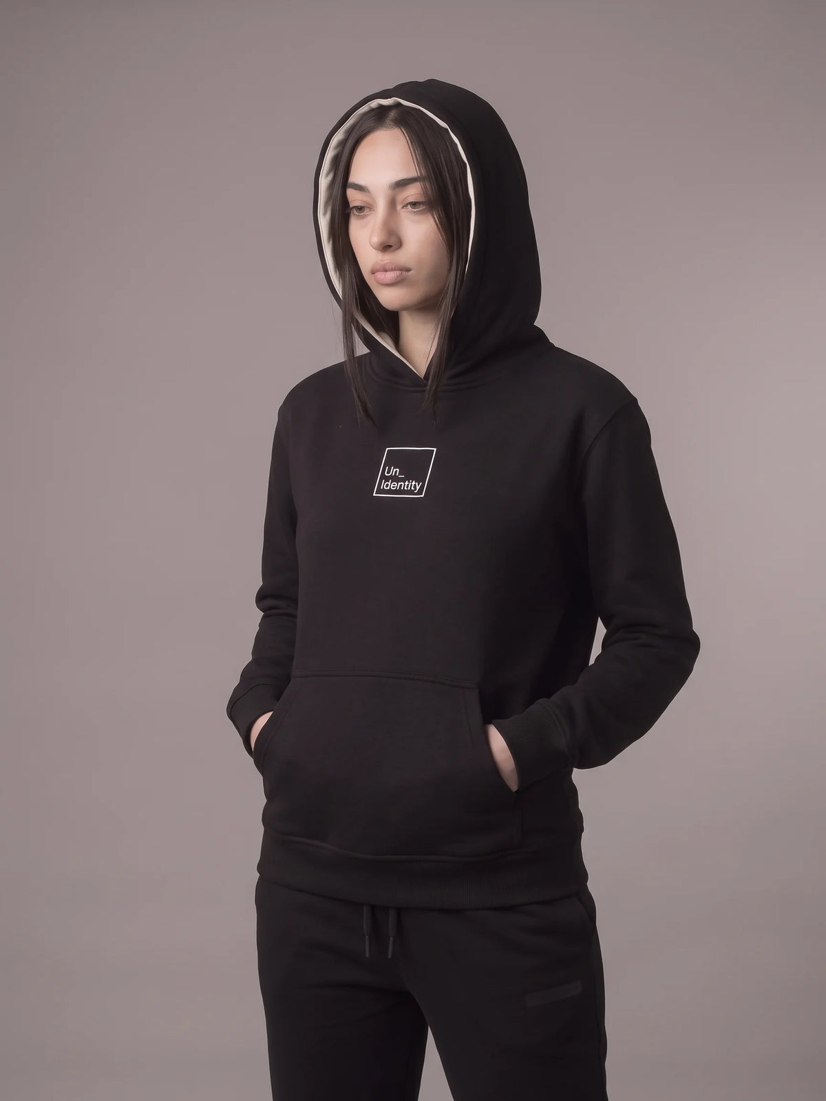 Black regular fit hoodie, Unidentity Core Regular Fit Hoodie, front view worn by woman with hood up showing the contrast lining, streetwear #color_black