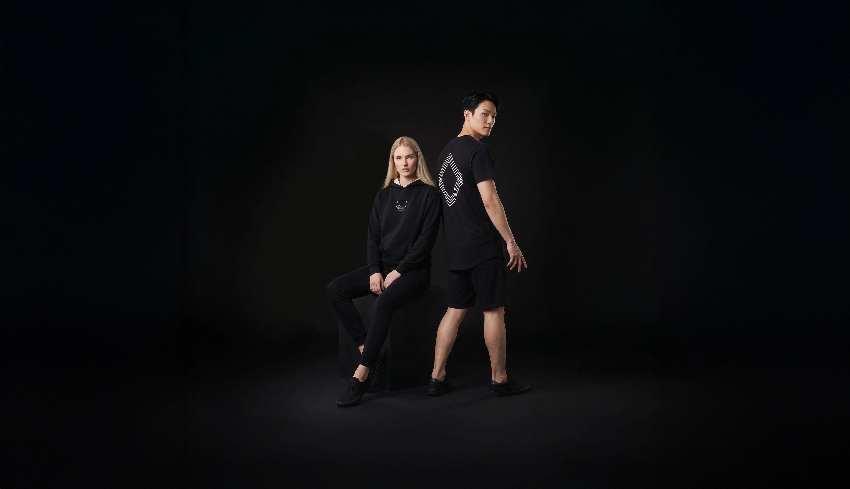 Two people in black outfits against a dark background