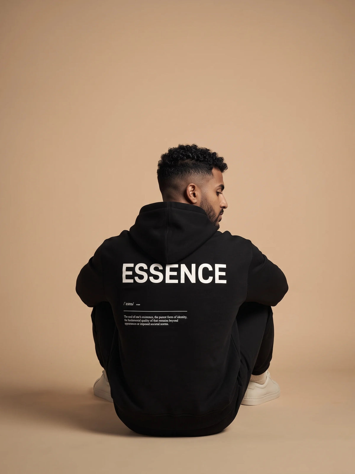 Black heavyweight hoodie in organic cotton, Unidentity Soul Hoodie, back view of the white ESSENCE print worn by seated man, UAE streetwear #color_black
