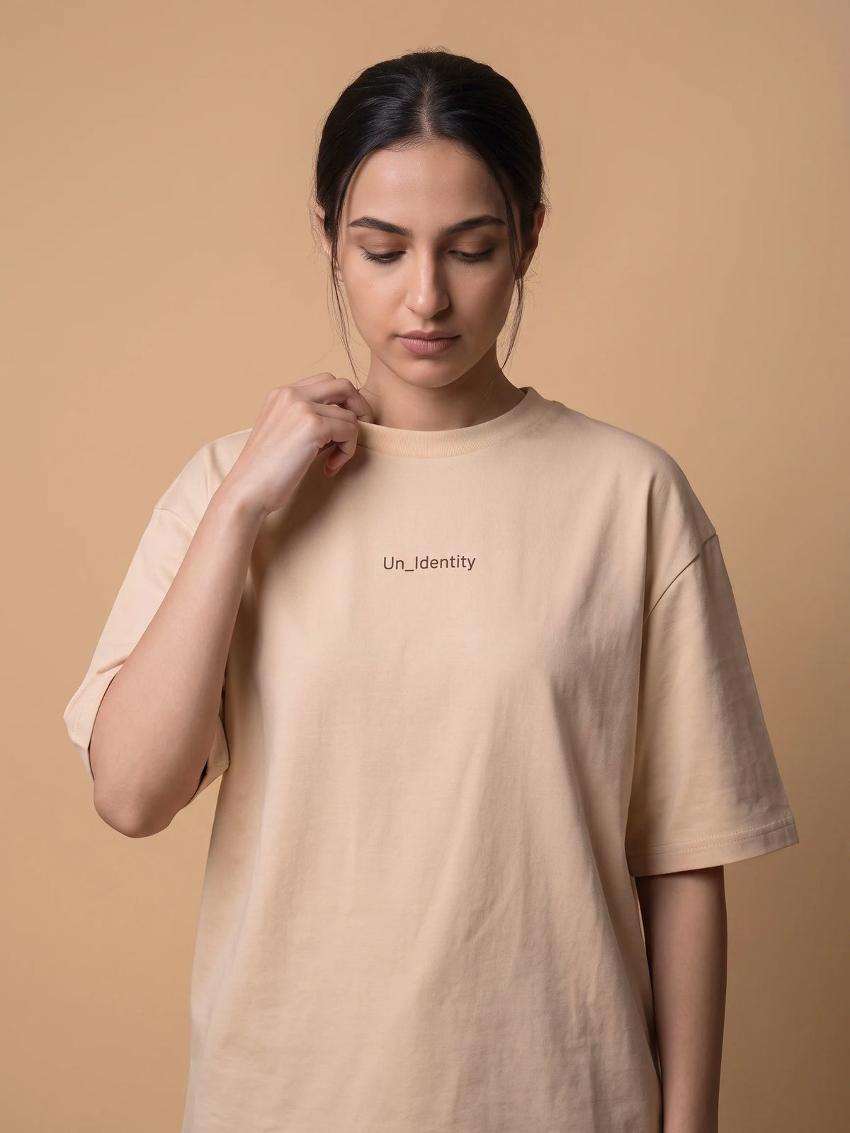 Beige organic cotton t-shirt, Unidentity Soul Oversized Tee, front close-up of the minimal chest logo worn by woman, sustainable streetwear #color_beige