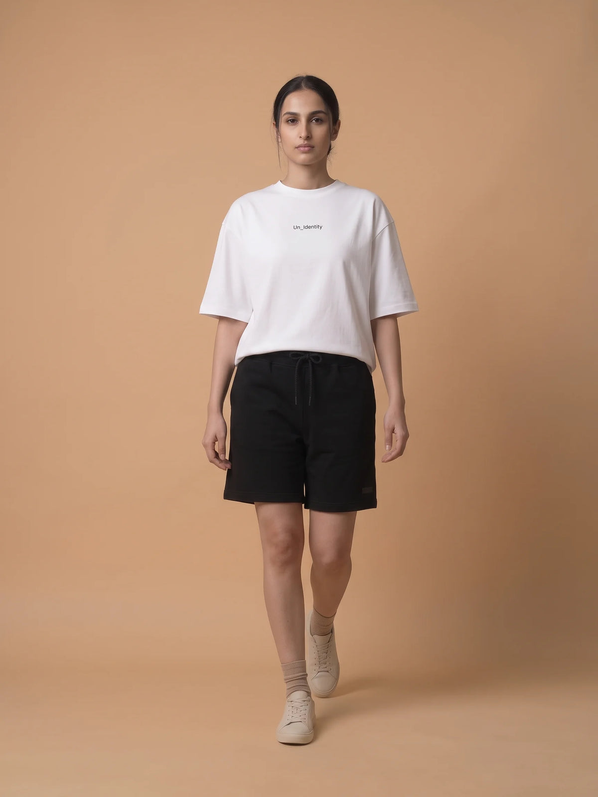 White oversized t-shirt in organic cotton, Unidentity Soul Tee, full-length front view worn by woman walking with black Core shorts, streetwear #color_white