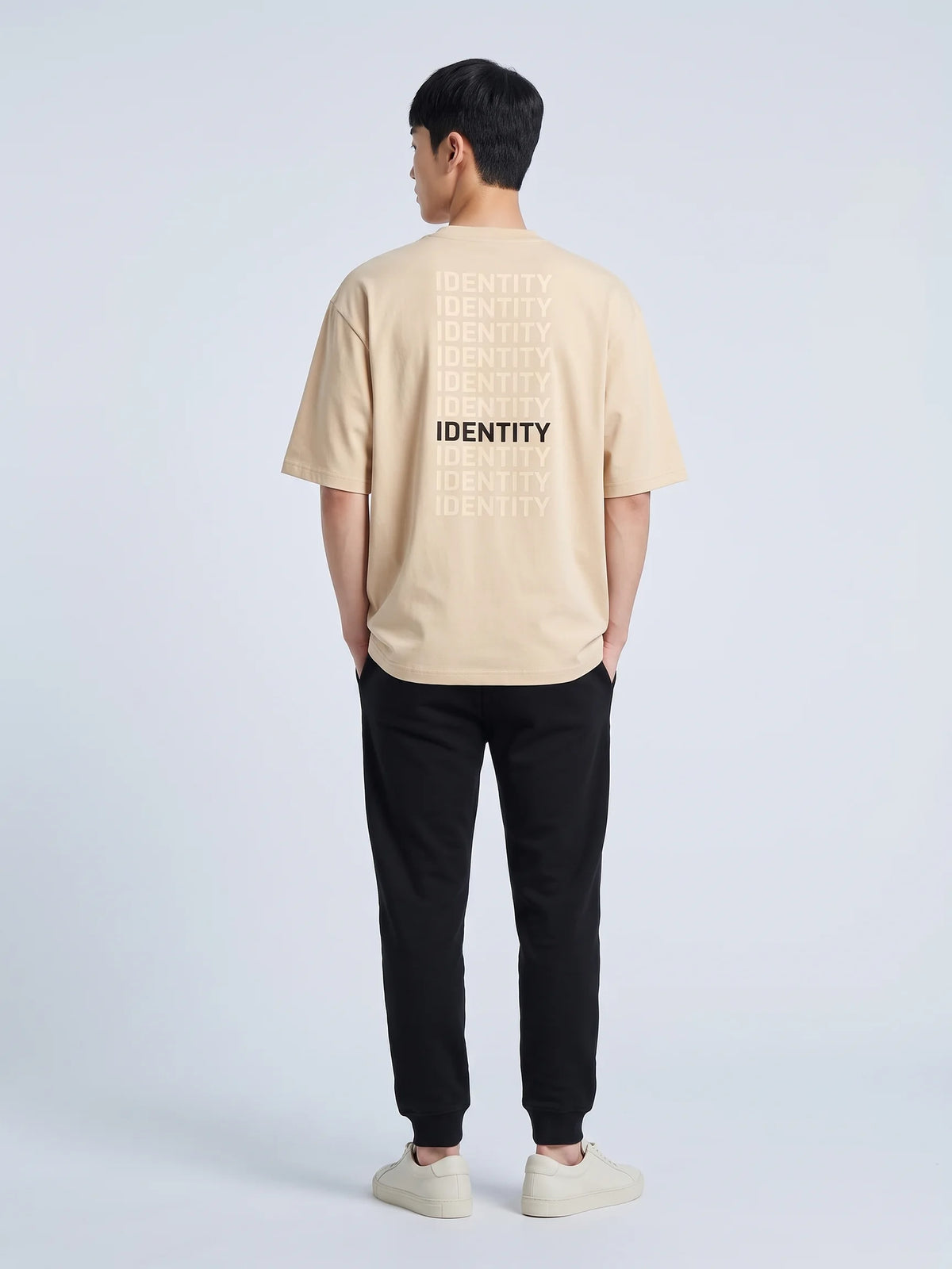 Beige oversized t-shirt in organic cotton, Unidentity Identity Tee, back view of the IDENTITY print, hands in joggers pockets, UAE streetwear #color_beige