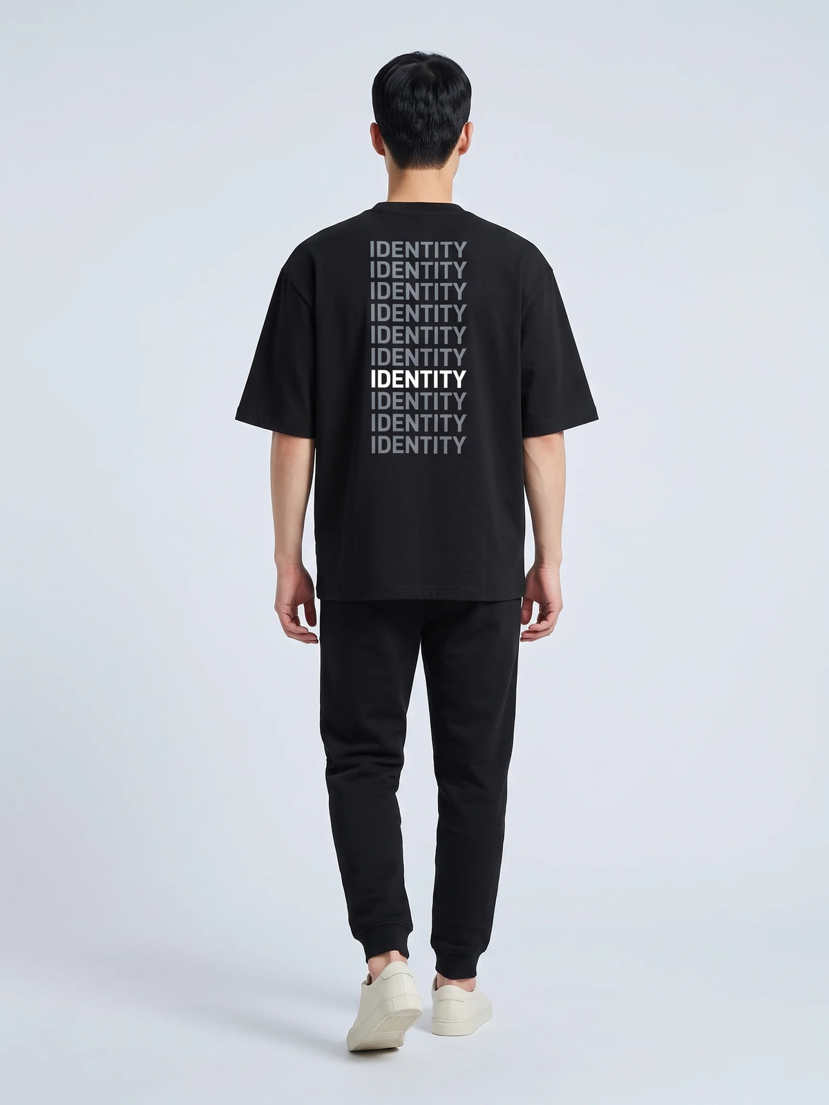 Black oversized t-shirt in organic cotton, Unidentity Identity Tee, full-length back view of the IDENTITY print worn by man walking, streetwear #color_black