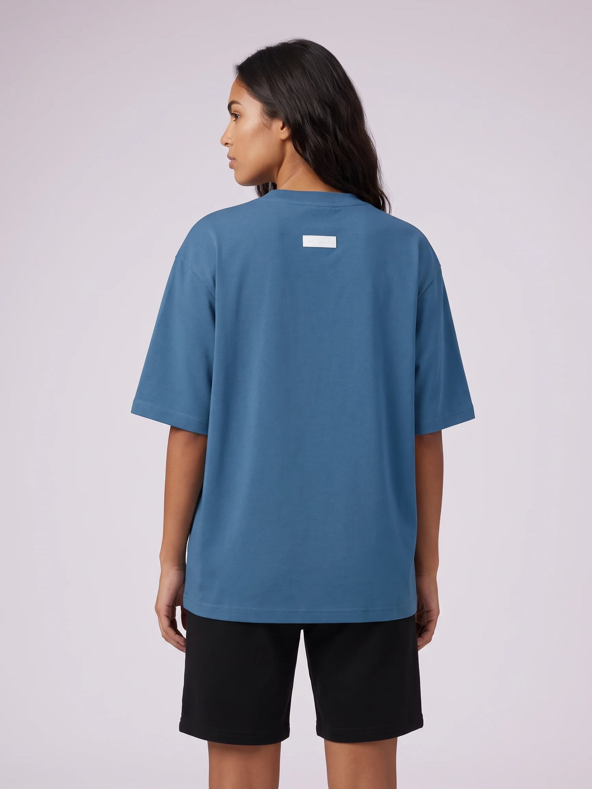 Blue oversized t-shirt, Unidentity Foundation Oversized Tee, upper back view worn by woman with the minimal 3D patch, sustainable streetwear #color_blue