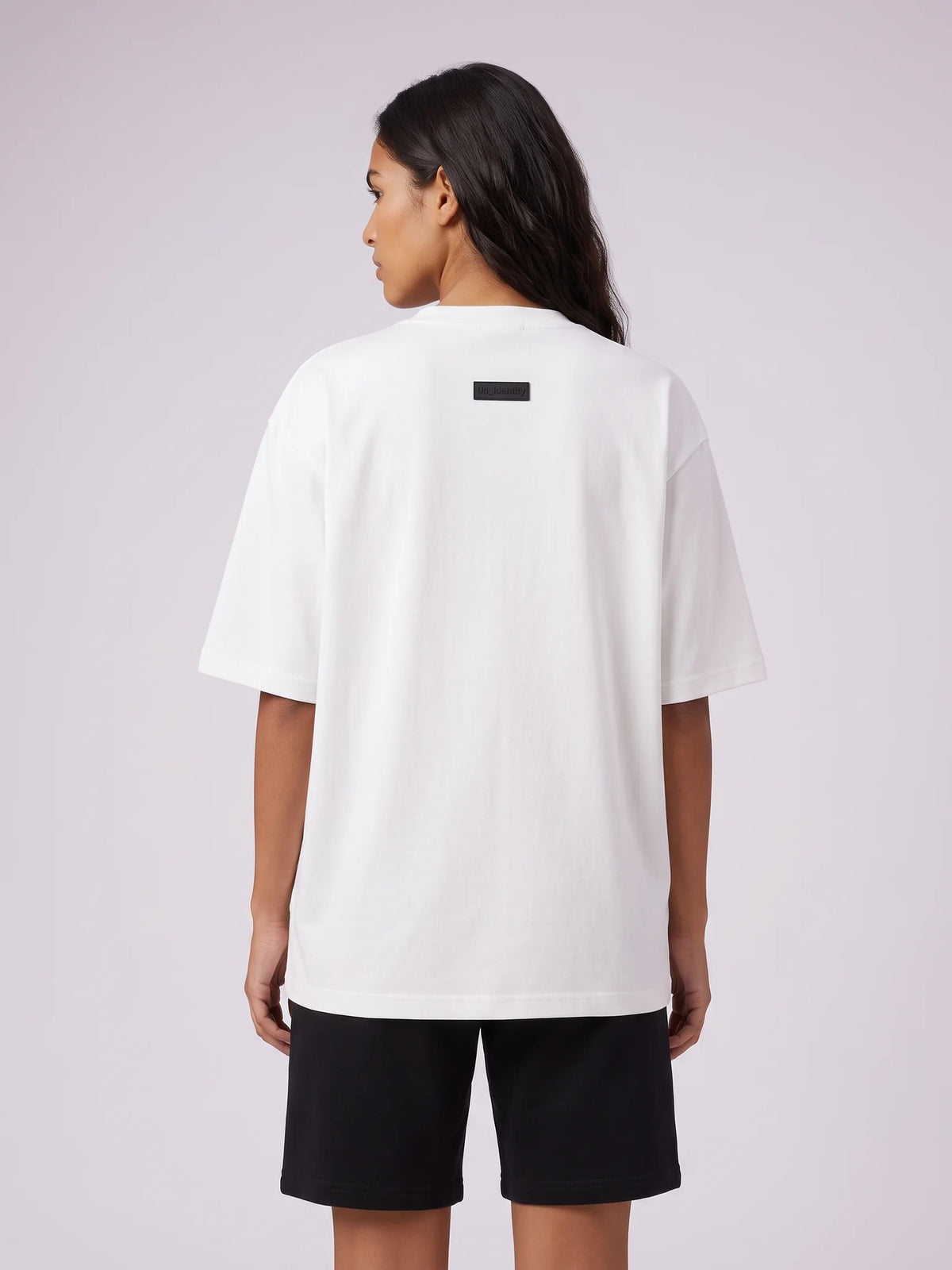 White oversized t-shirt, Unidentity Foundation Oversized Tee, upper back view worn by woman with the minimal black 3D patch below the collar #color_white