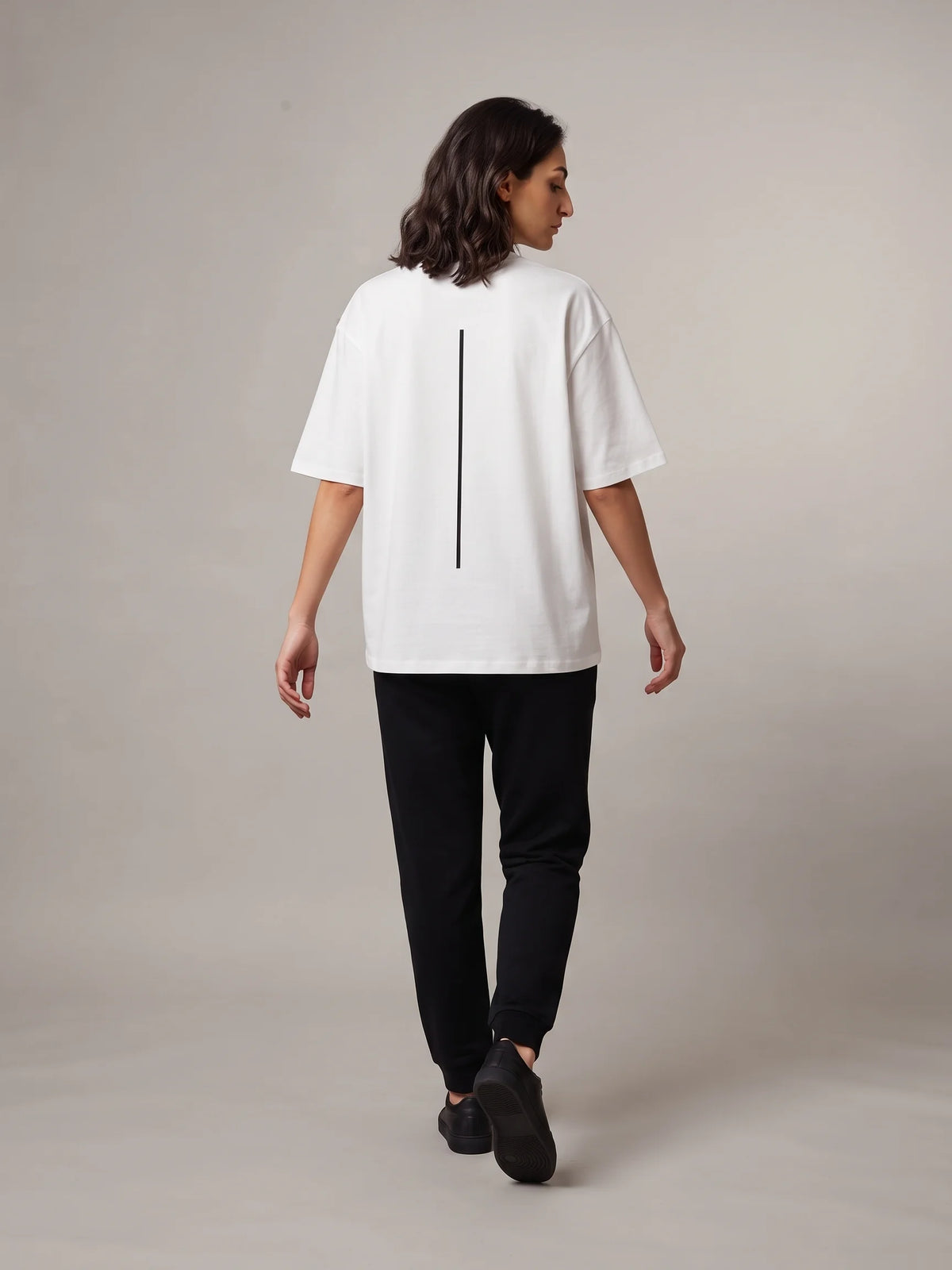 White oversized t-shirt in organic cotton, Unidentity Trace Tee, full-length back view of a woman walking in Core joggers, sustainable fashion #color_white