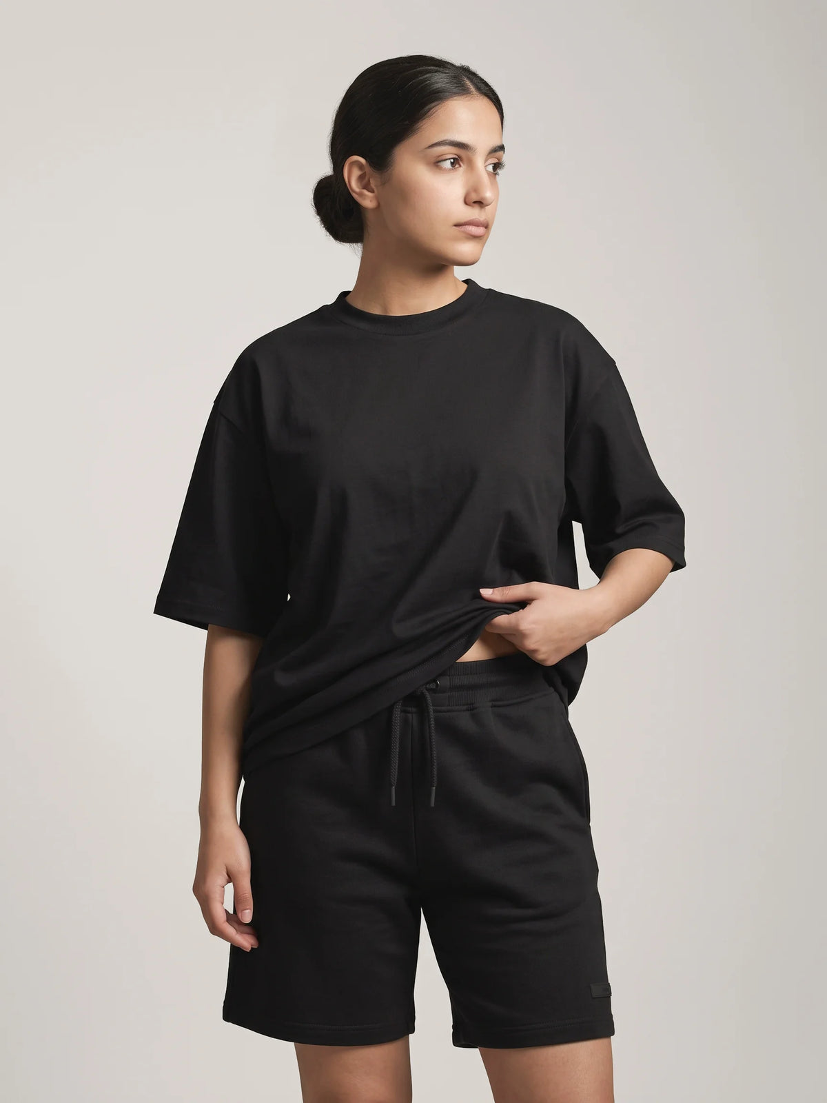 Black oversized t-shirt, Unidentity You Tee, front view worn by woman showing the crew neck, styled with black Core shorts, streetwear #color_black