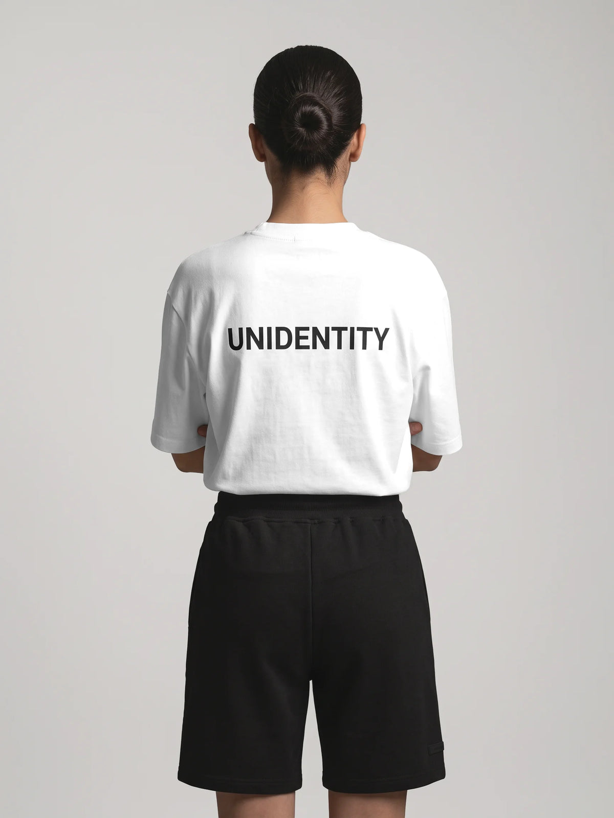 White oversized t-shirt, Unidentity You Oversized Tee, back view worn by woman showing the bold black UNIDENTITY logo, 210gsm streetwear #color_white
