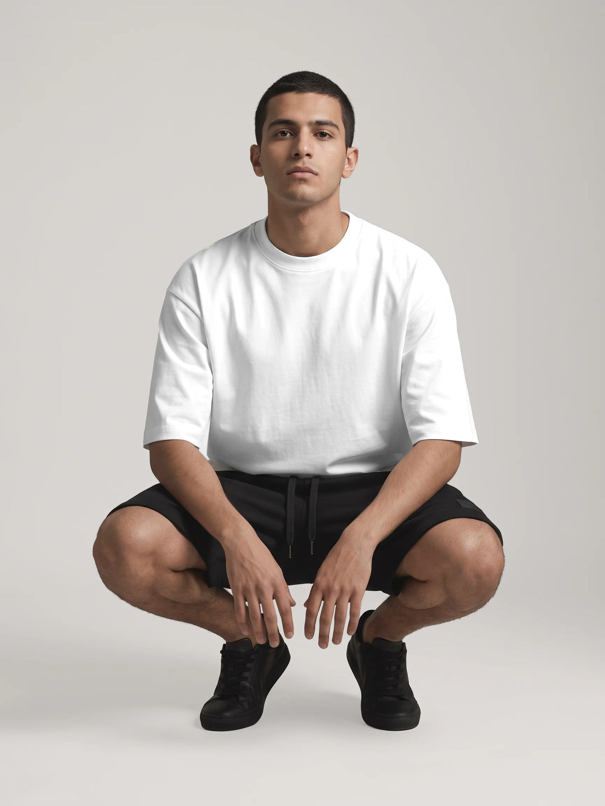 White oversized t-shirt in organic cotton, Unidentity You Oversized Tee, front view of a crouching man showing the dropped shoulders, 210gsm #color_white