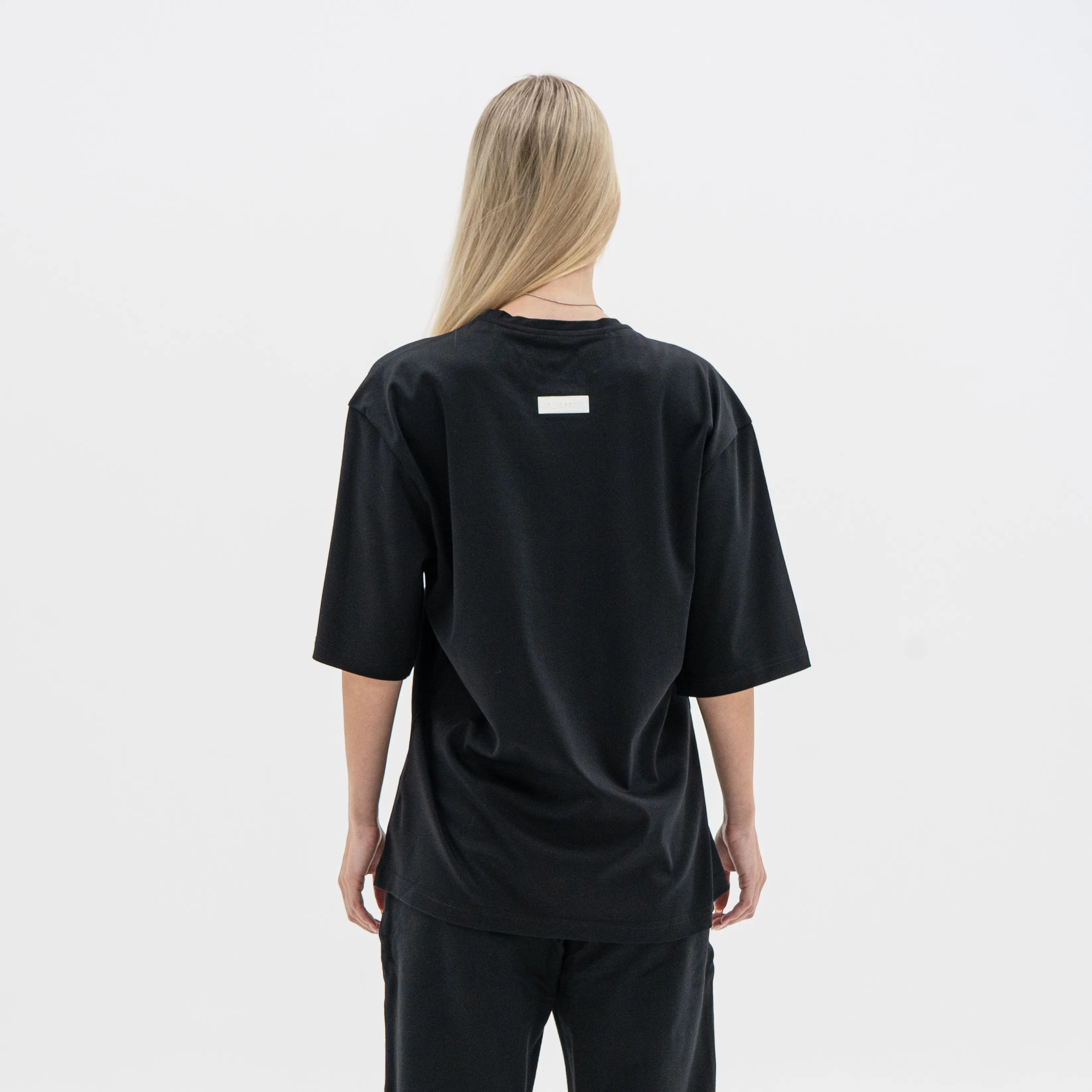Person wearing a black oversized t-shirt with a small white label on the back against a plain background. #color_black