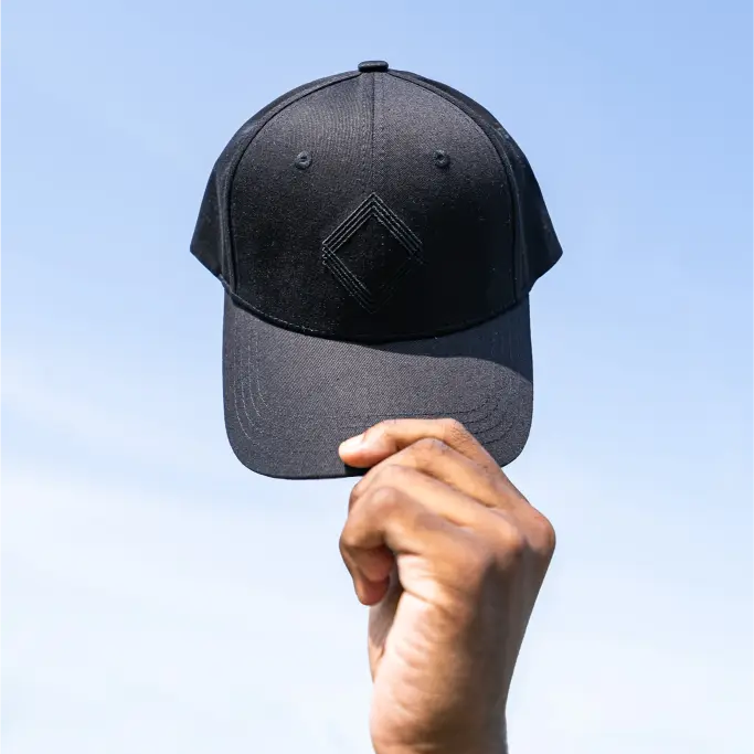 Black Unidentity baseball cap held by hand against clear blue sky