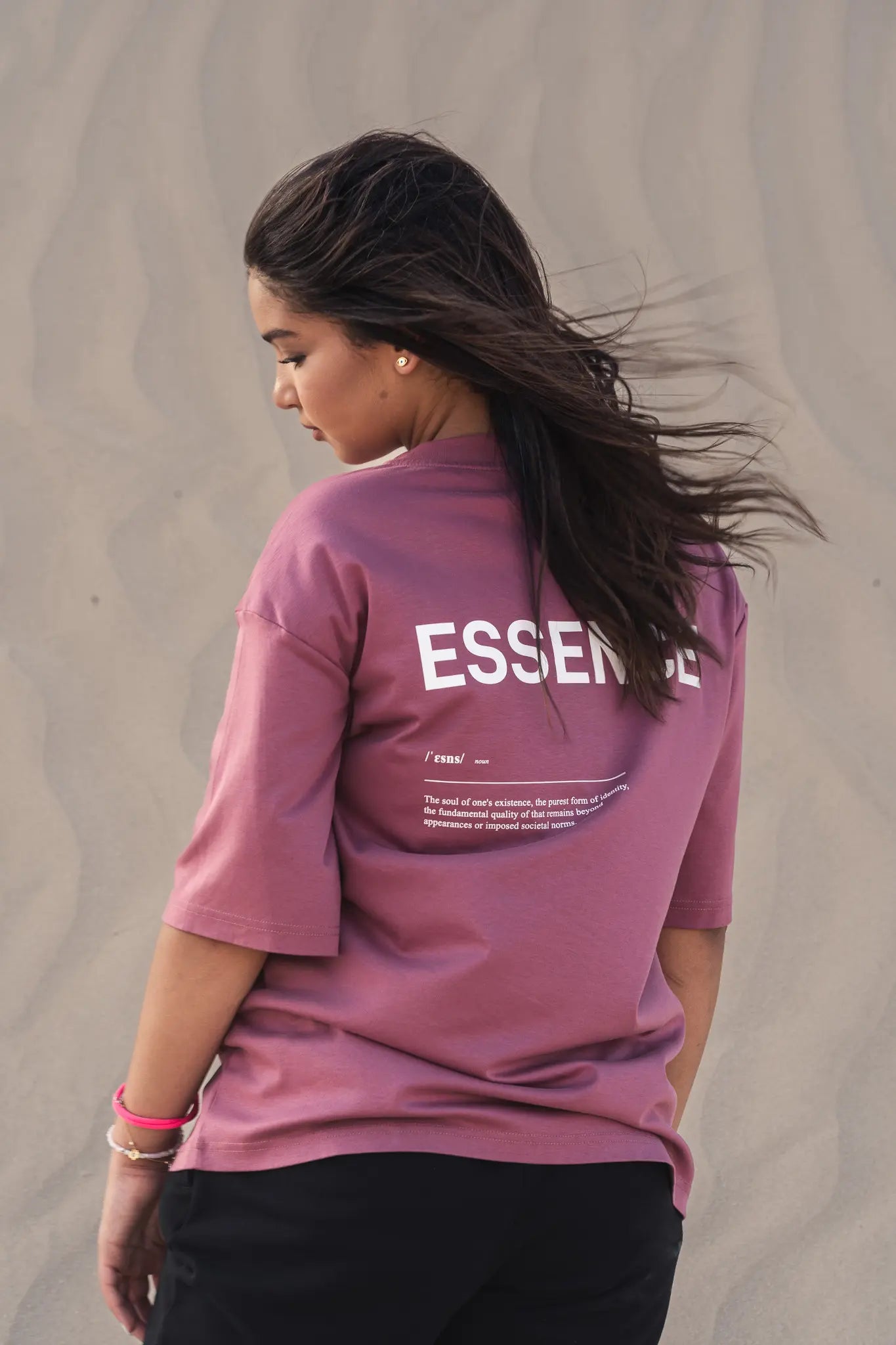 Person wearing Unidentity purple tee with ESSENCE printed on the back at the desert. #color_plum