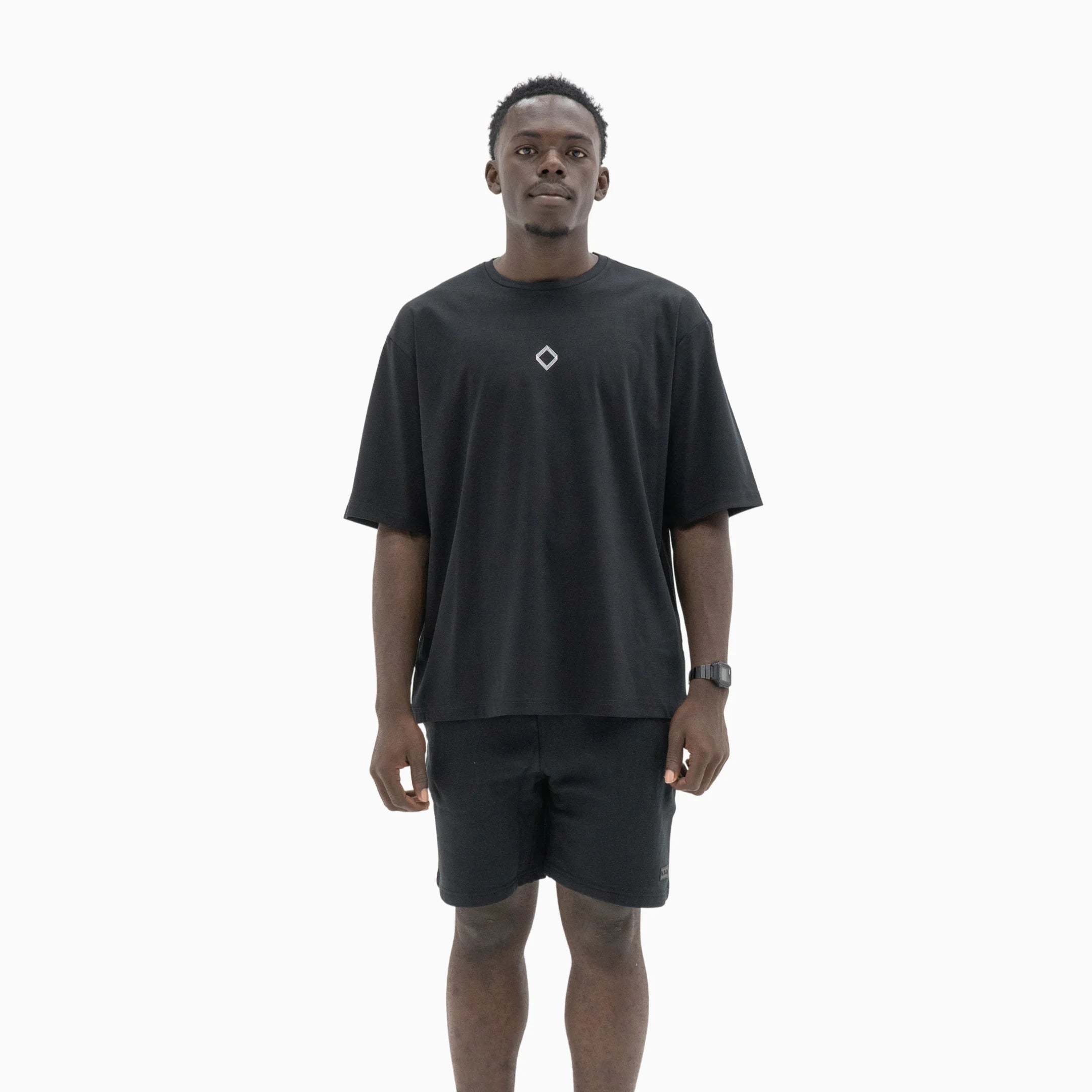 Person wearing a black t-shirt with a white logo on the chest against a plain background. #color_black