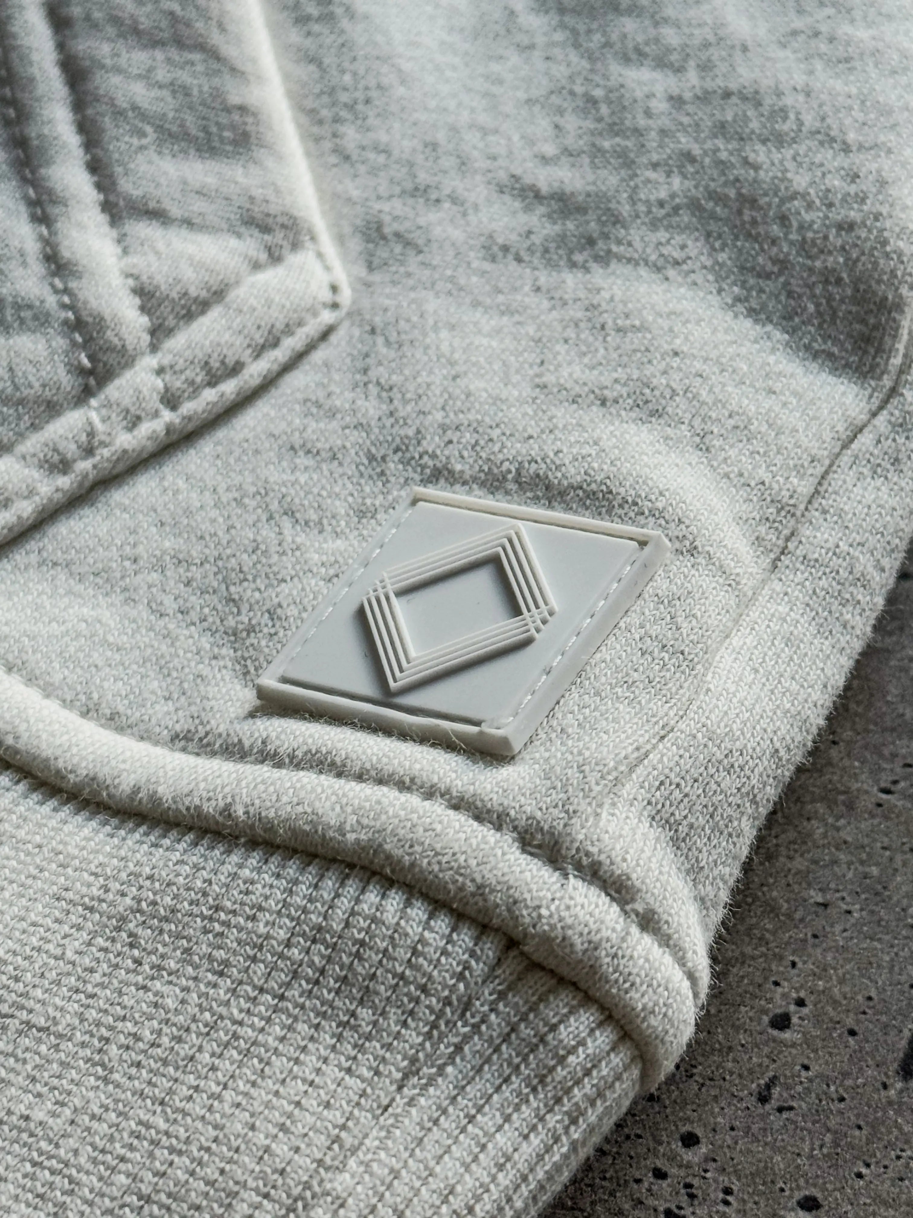 Close-up of a textured white fabric with a small rectangular Gem Unidentity patch logo on a concrete surface