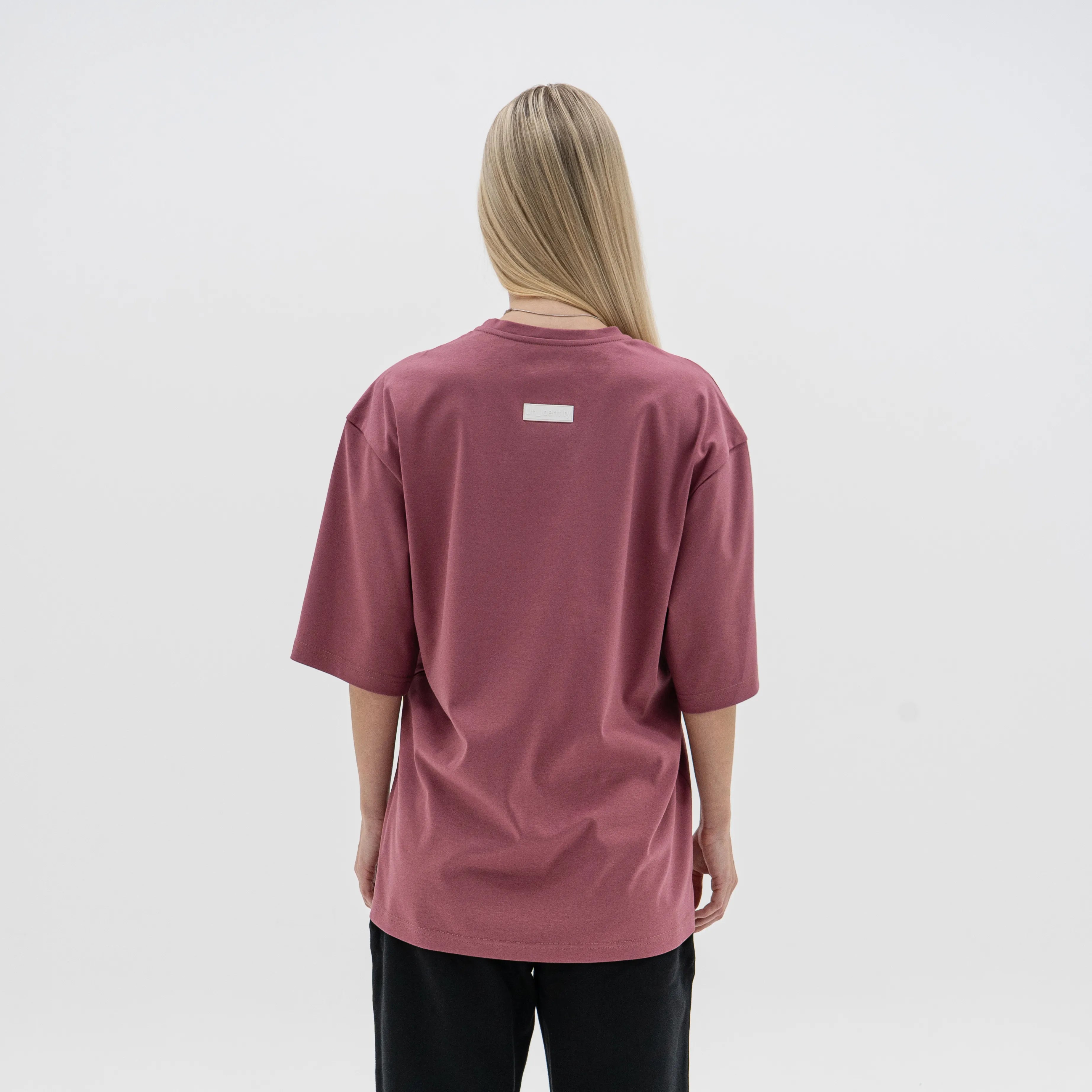 Person wearing a maroon t-shirt with a small logo on the back against a white background. #color_plum