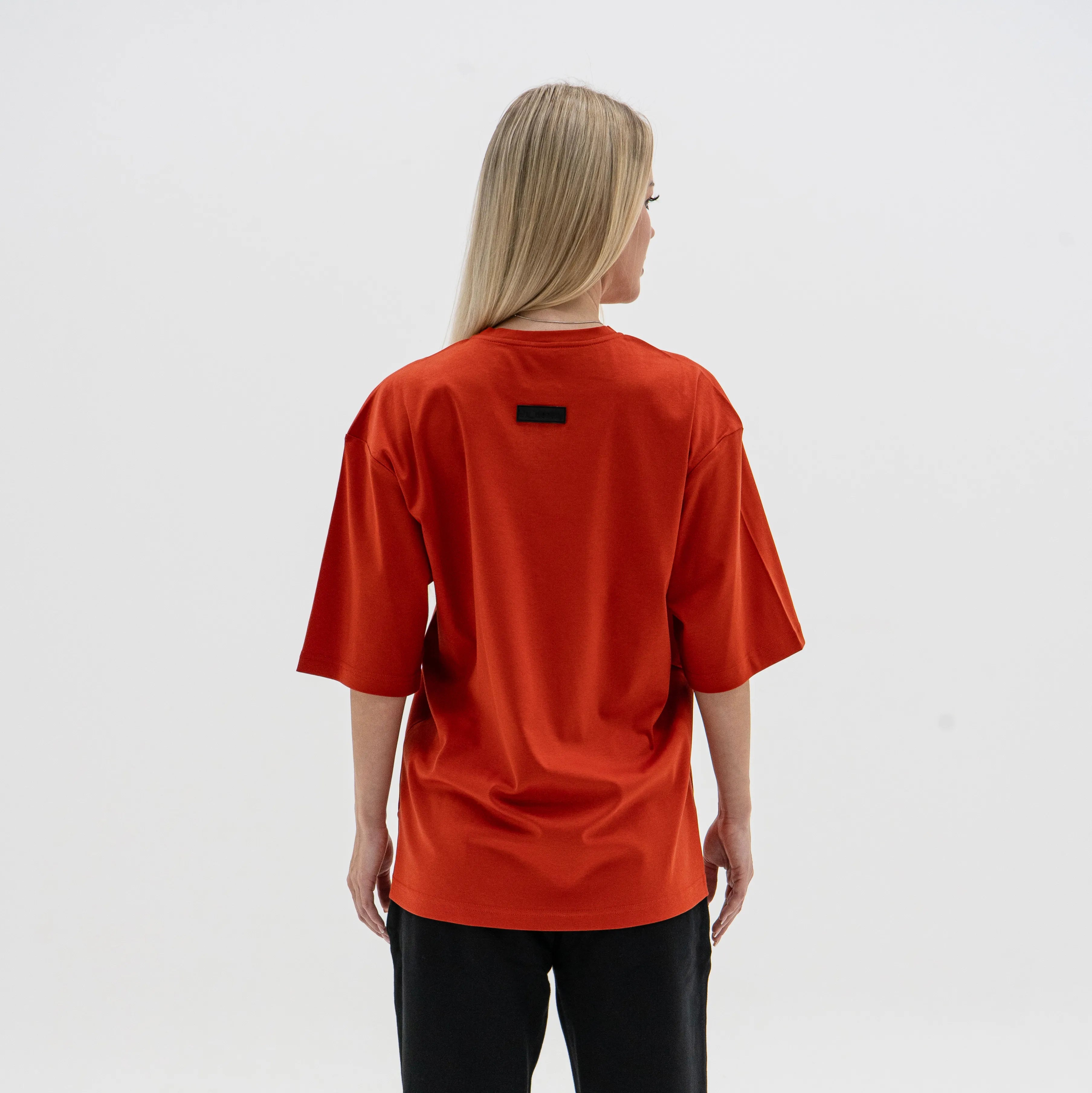 Person wearing an red t-shirt with a small black logo on the back, standing against a plain white background. #color_red