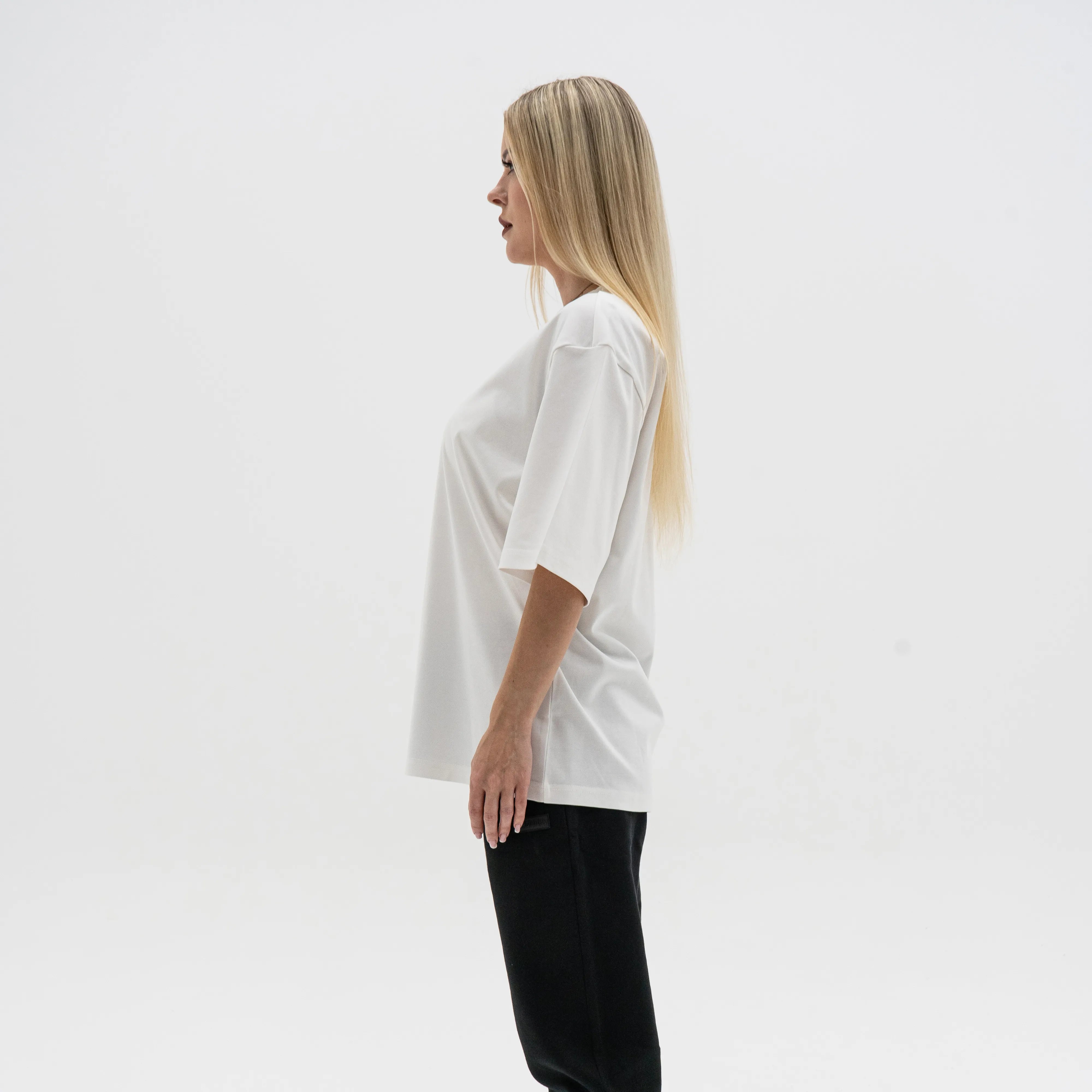 Woman wearing a white oversized t-shirt against a plain background. #color_white