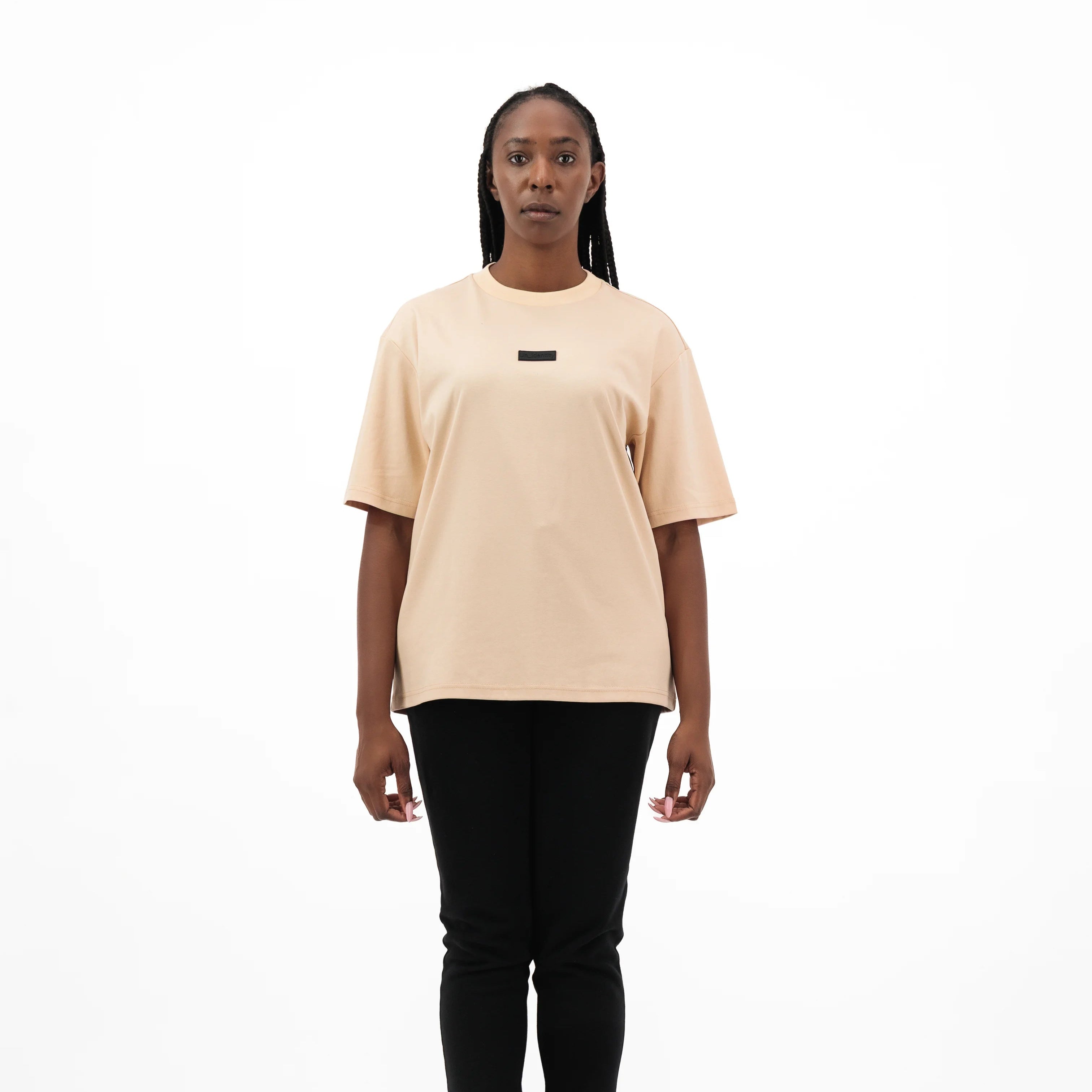 Woman wearing beige tee with black 3D Unidentity patch on the chest and black pants. #color_beige
