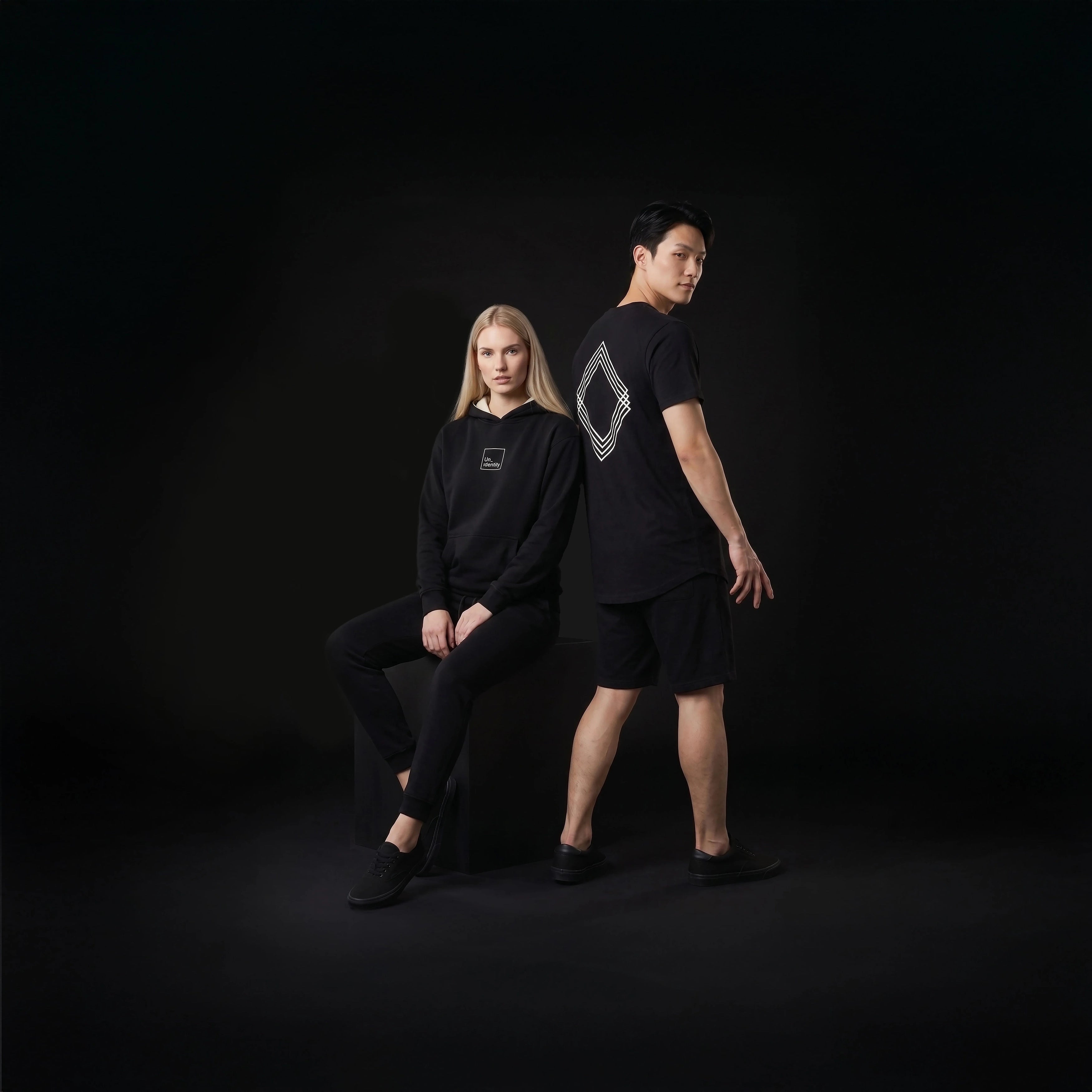 Two people wearing black outfits against a dark background
