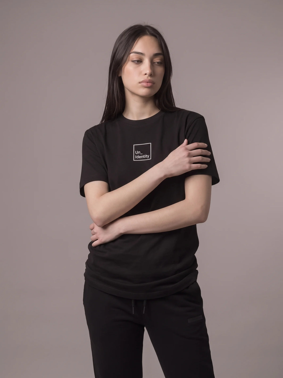 Black 210gsm long fit t-shirt in organic cotton, Unidentity Core Tee, front view worn by woman with white boxed chest logo, streetwear brand in Dubai #color_black