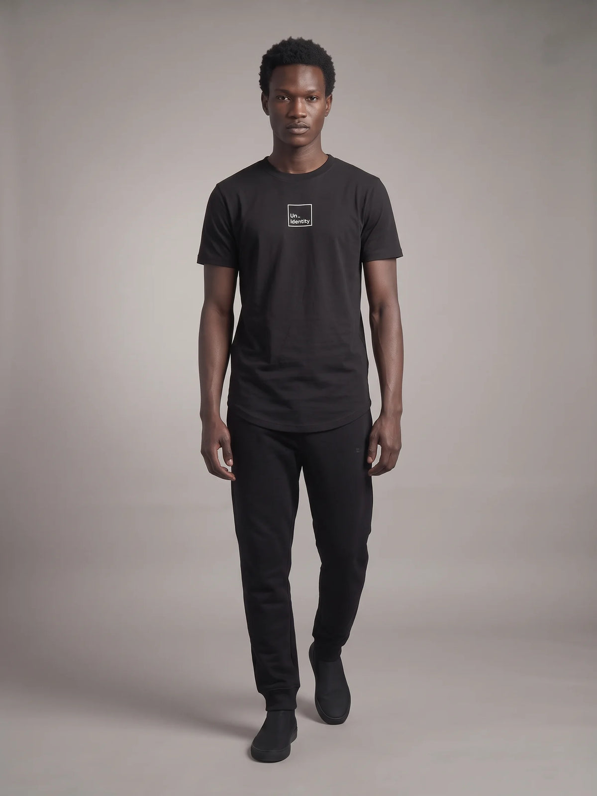 Black organic cotton t-shirt, Unidentity Core Tee, full-length front view on man styled with black Core Regular Fit Joggers, streetwear from Dubai #color_black