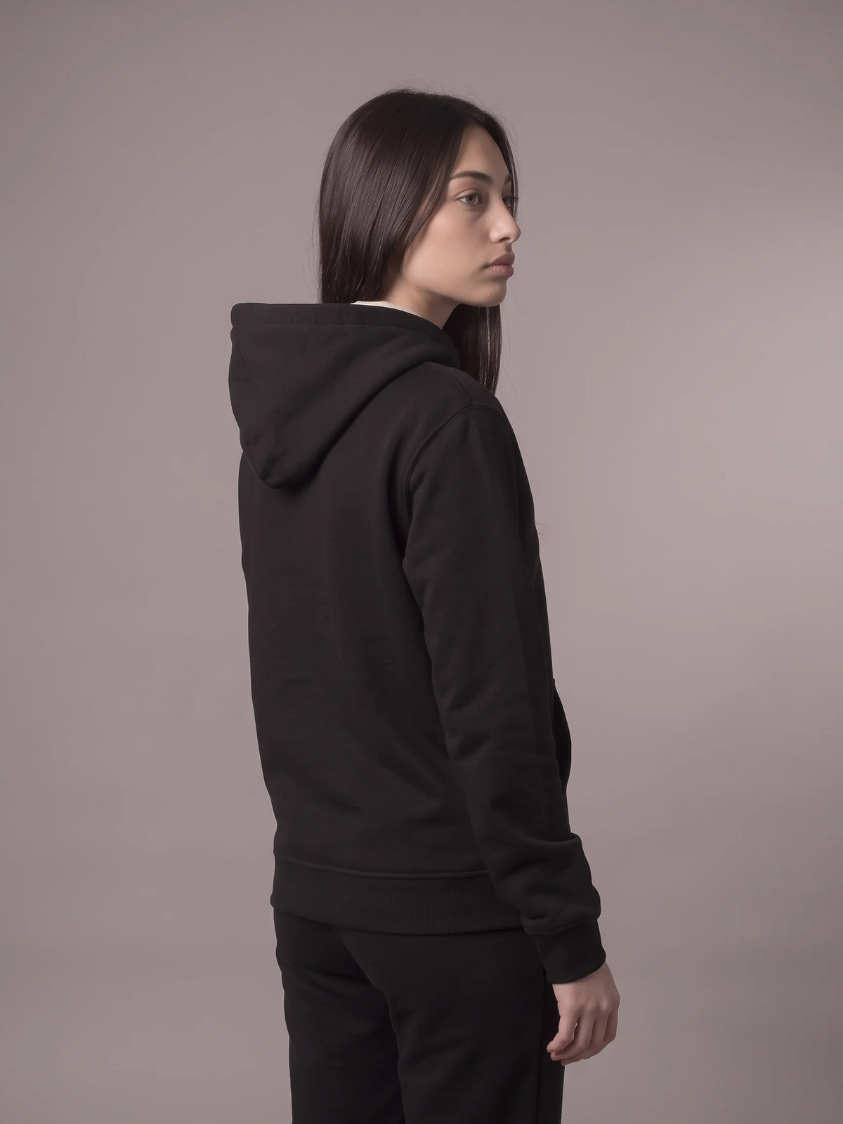 Black organic cotton hoodie, Unidentity Core Hoodie, back view worn by woman with hood down showing the plain back and ribbed hem, UAE streetwear #color_black