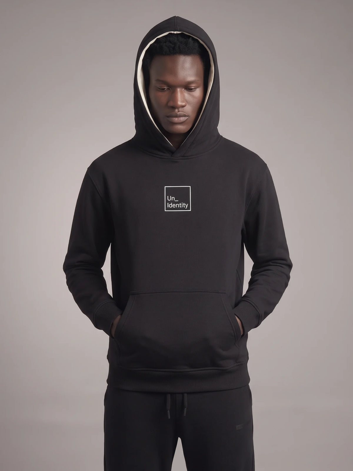 Black heavyweight hoodie in organic cotton, Unidentity Core Hoodie, front view on man with hood up and boxed chest logo, 390gsm streetwear from Dubai #color_black