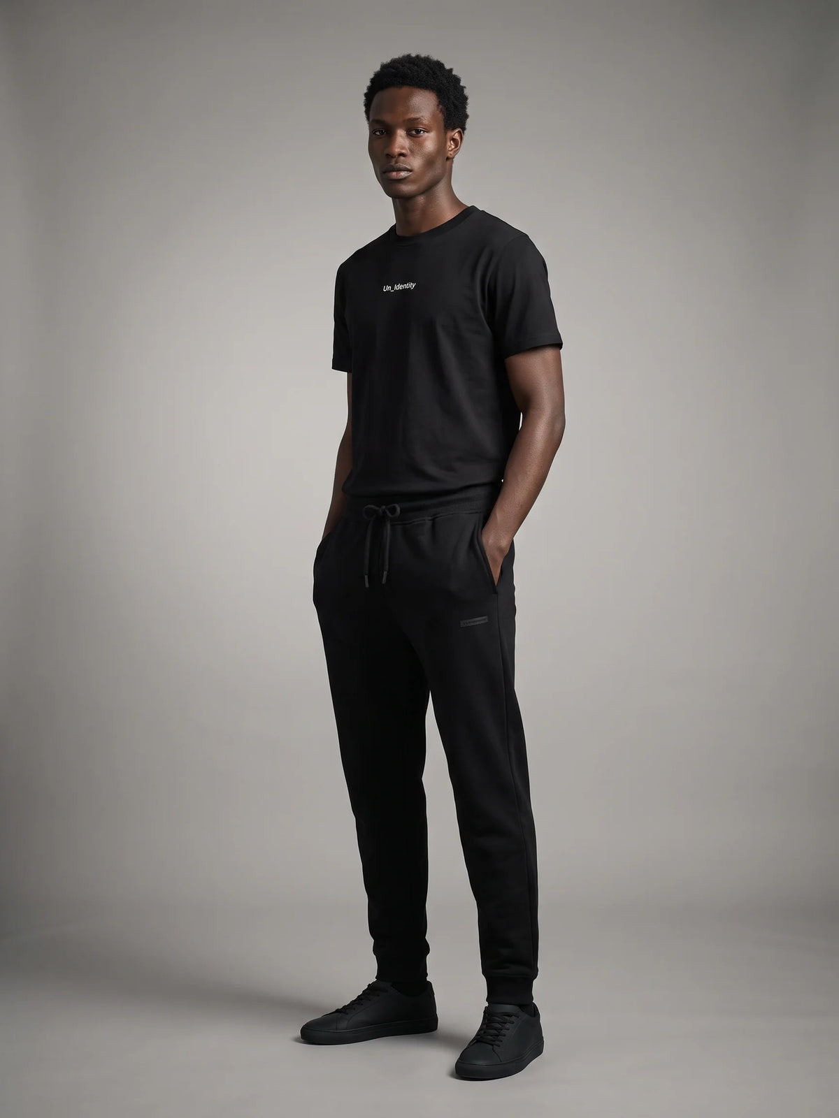 Black organic cotton t-shirt, Unidentity Gem Long Fit Tee, full-length front view on man, hands in pockets, with black Core joggers, streetwear #color_black