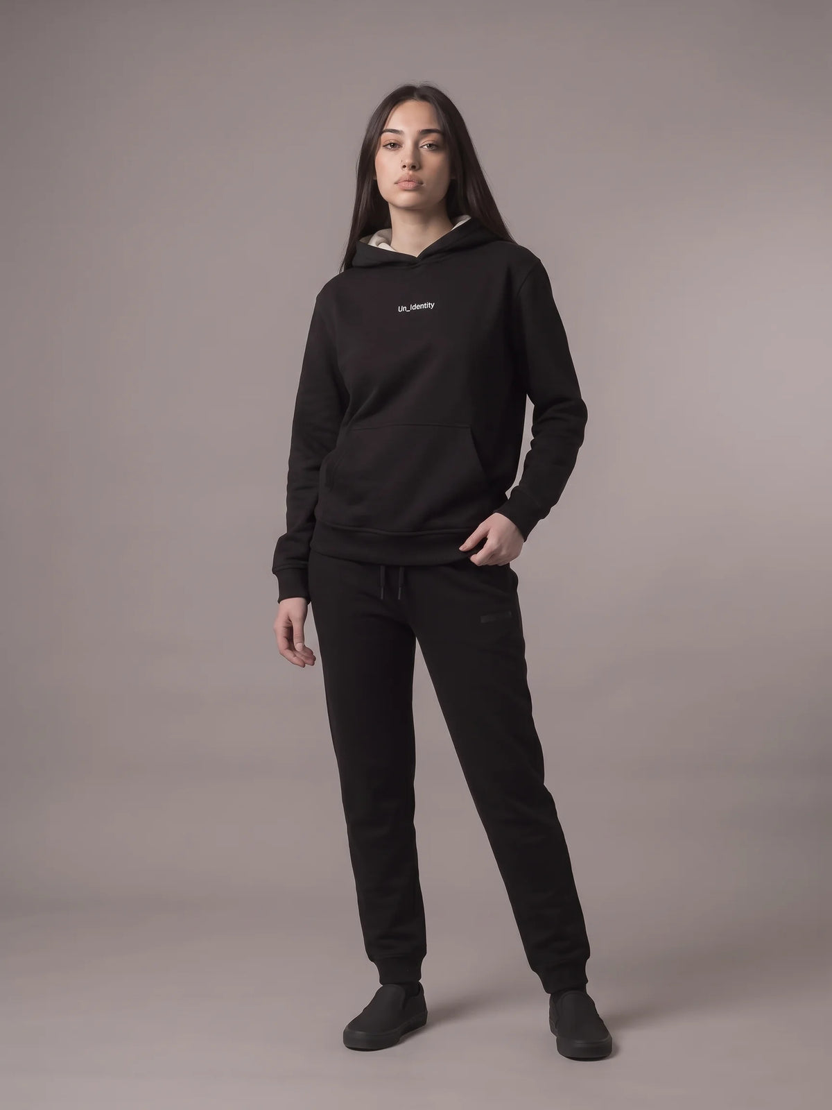Black regular fit hoodie in organic cotton, Unidentity Gem Hoodie, full-length front view on woman with black Core joggers, sustainable streetwear #color_black