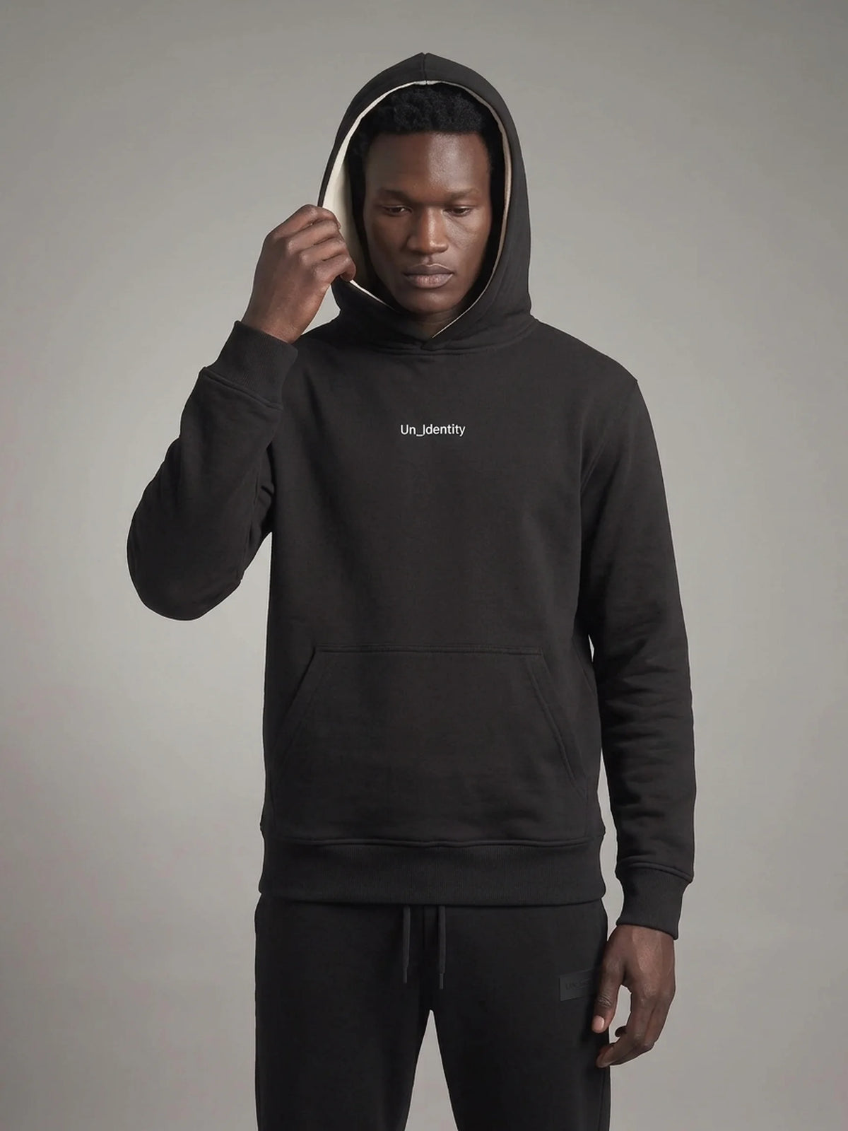 Black heavyweight hoodie, Unidentity Gem Hoodie, front view on man pulling up the hood, UAE streetwear #color_black