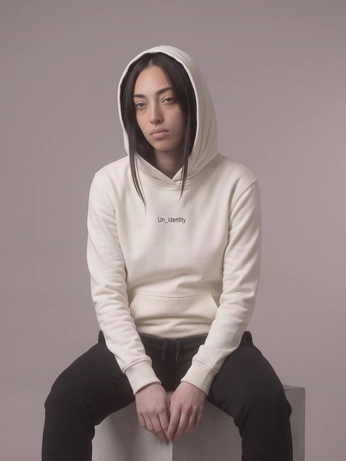 White heavyweight hoodie, Unidentity Gem Hoodie, seated front view worn by woman with hood up and Un_Identity wordmark, streetwear from Dubai #color_white