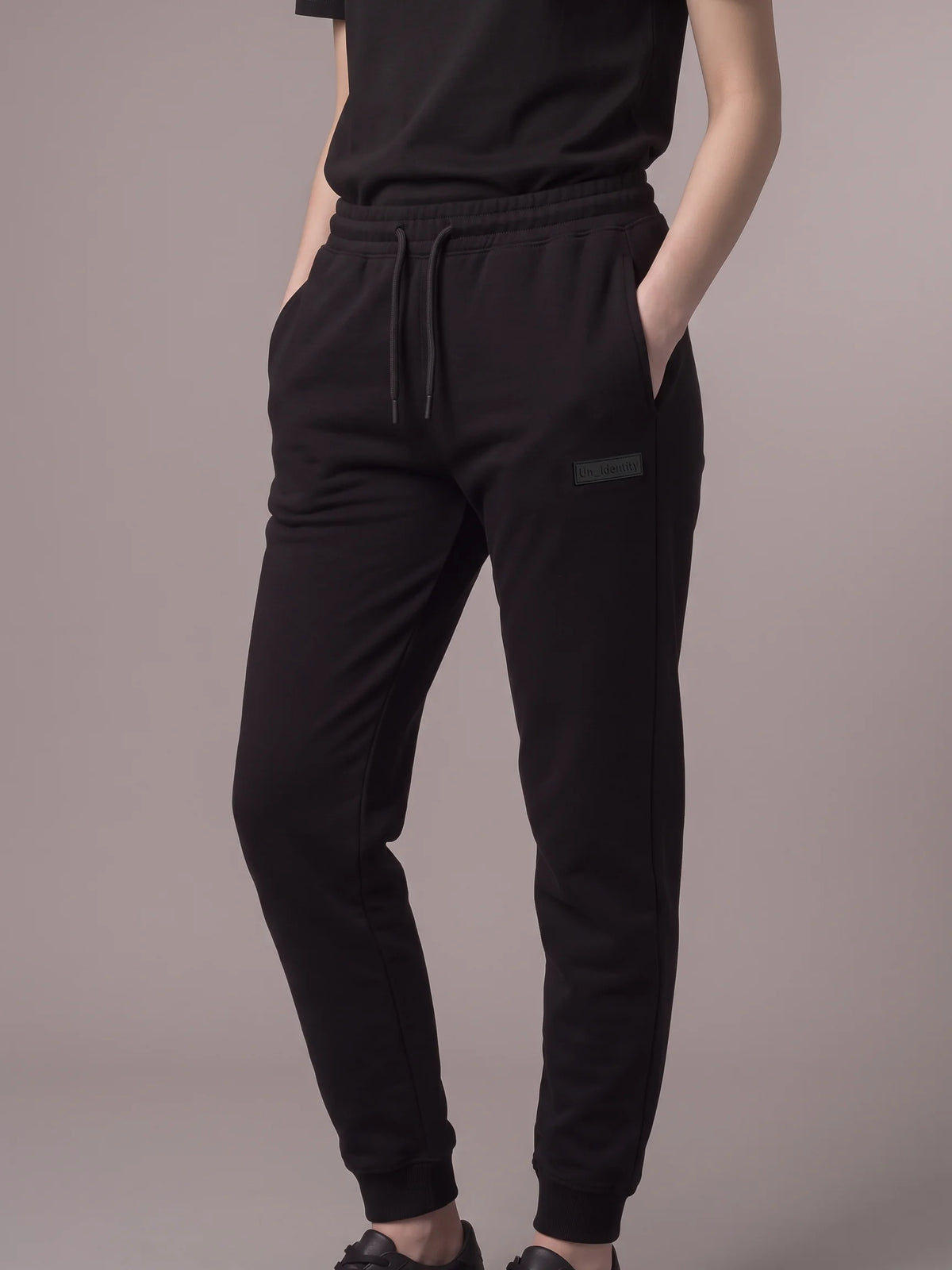 Black joggers in organic cotton, Unidentity Core Joggers, front view worn by woman with hands in side pockets, 390gsm streetwear from the UAE #color_black
