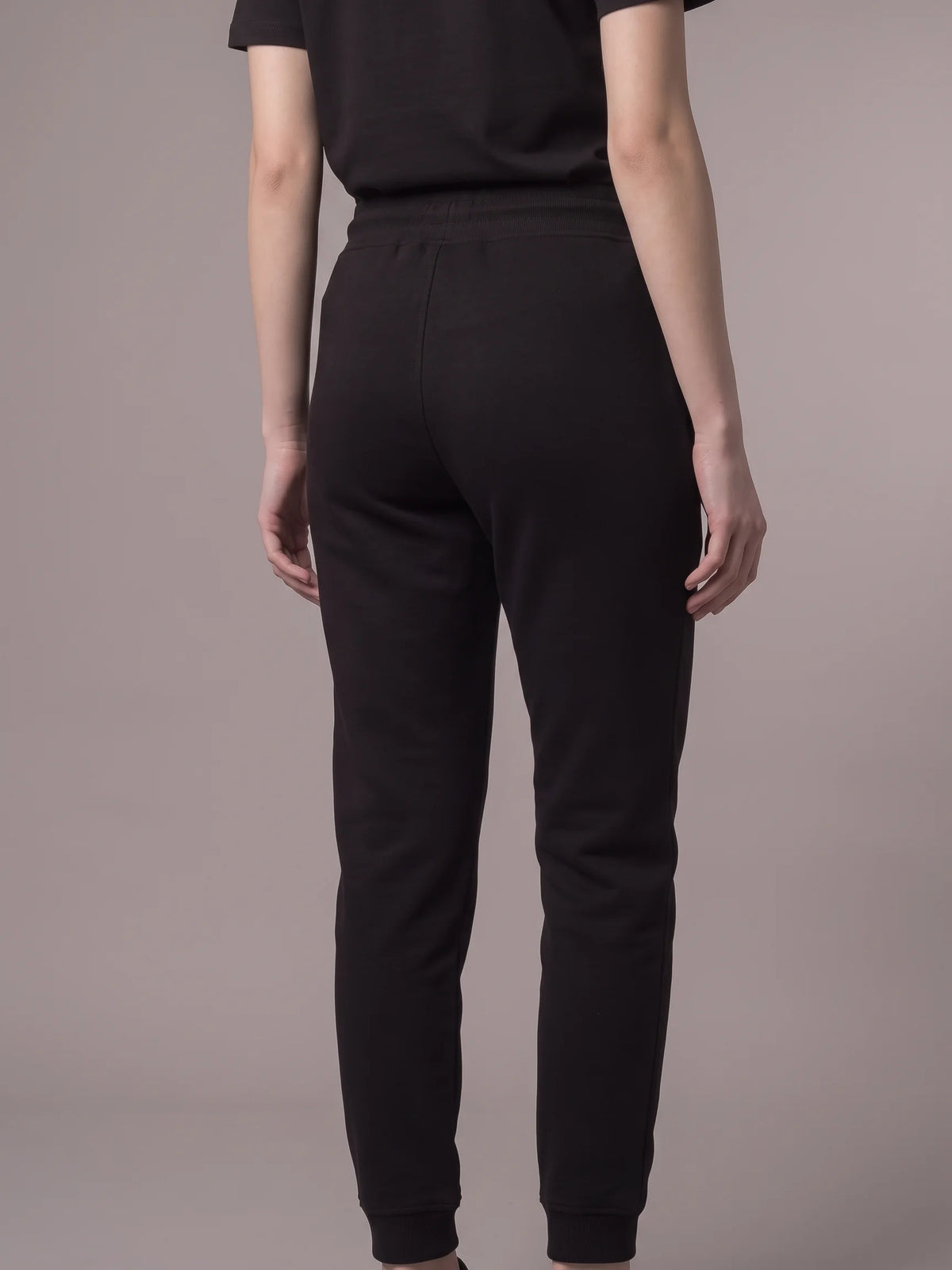 Black joggers in organic cotton, Unidentity Core Joggers, back view worn by woman showing the tapered leg and ribbed cuffs, sustainable fashion #color_black