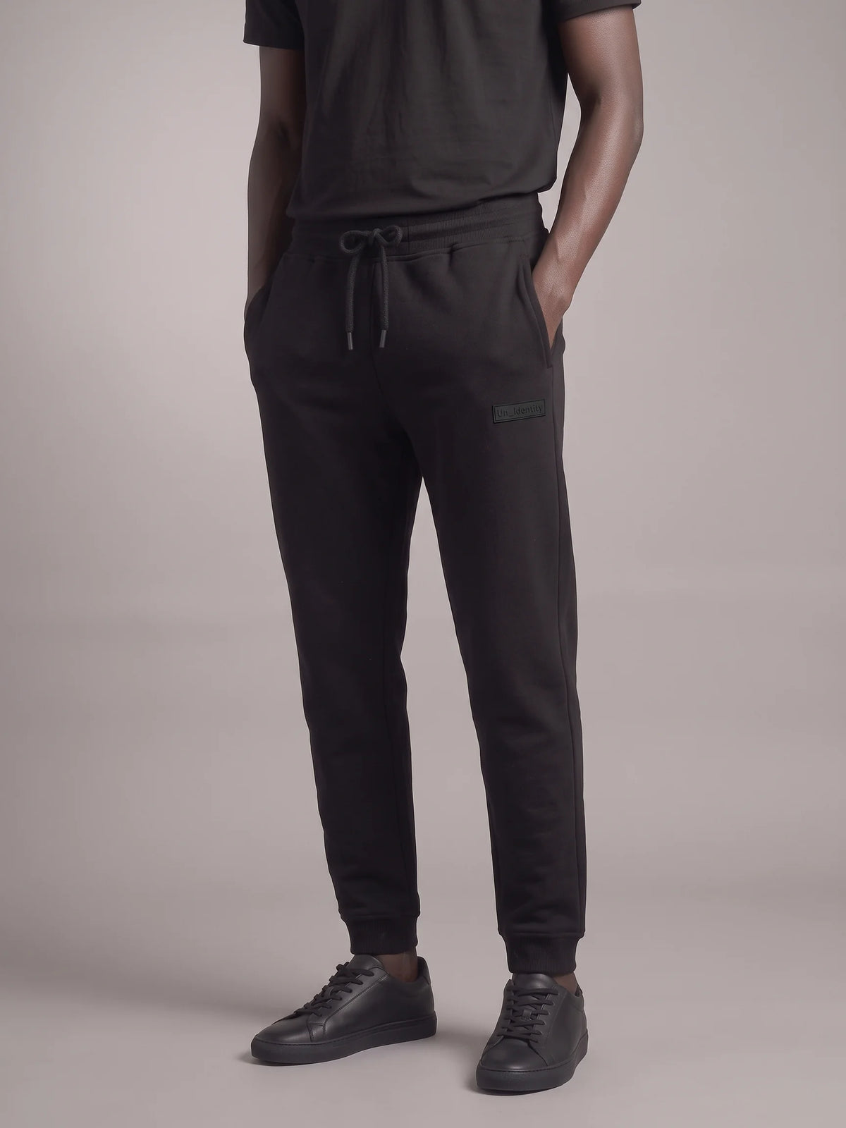 A person wearing black jogger sweatpants with a drawstring waist, paired with a black t-shirt and black sneakers, shown from the chest down against a neutral studio background. #color_black