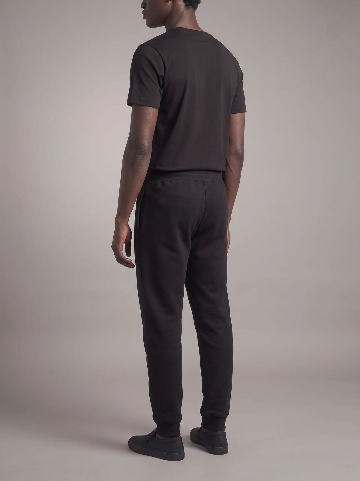 Black heavyweight sweatpants, Unidentity Core Regular Fit Joggers, full-length back view worn by man with a black tee, streetwear brand in Dubai #color_black
