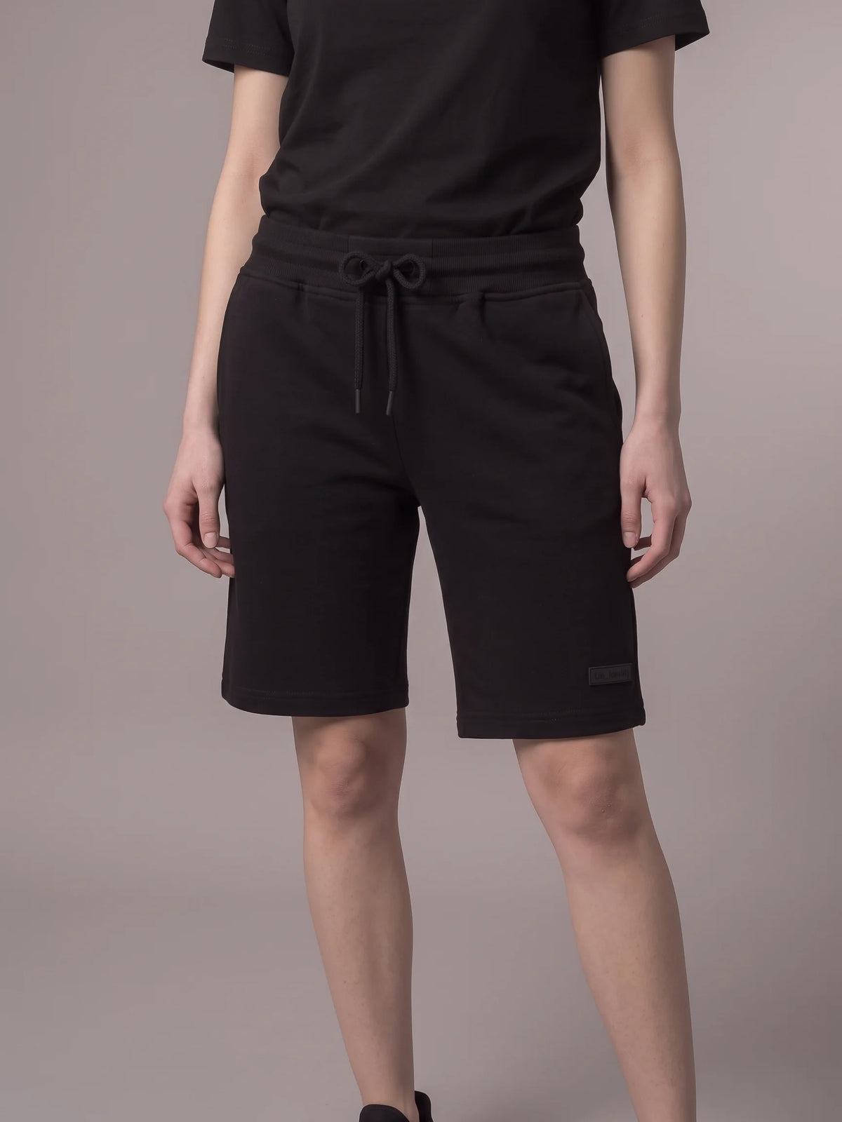Black cotton shorts, Unidentity Core Regular Fit Shorts, front view worn by woman showing the knee-length cut, sustainable streetwear #color_black