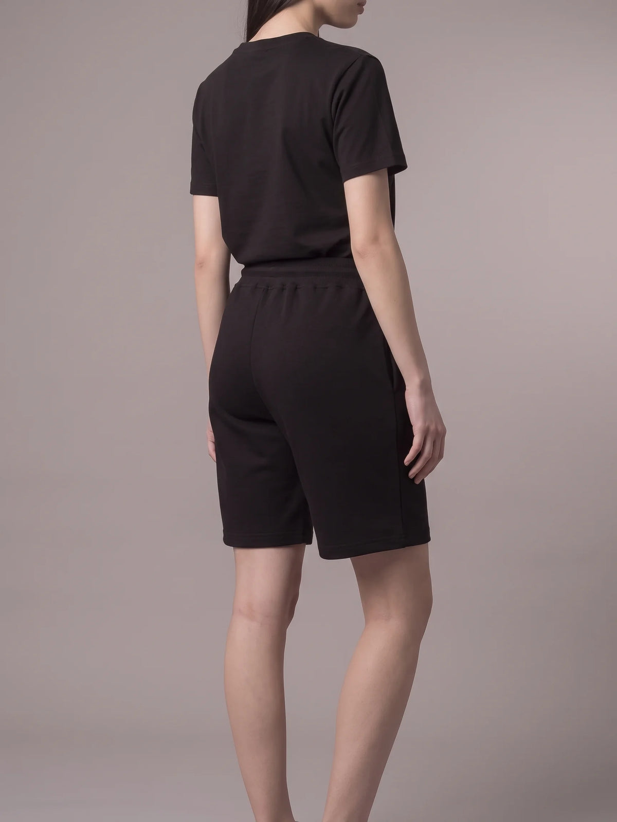 Black cotton shorts, Unidentity Core Regular Fit Shorts, back view worn by woman styled with a black tee, 390gsm #color_black