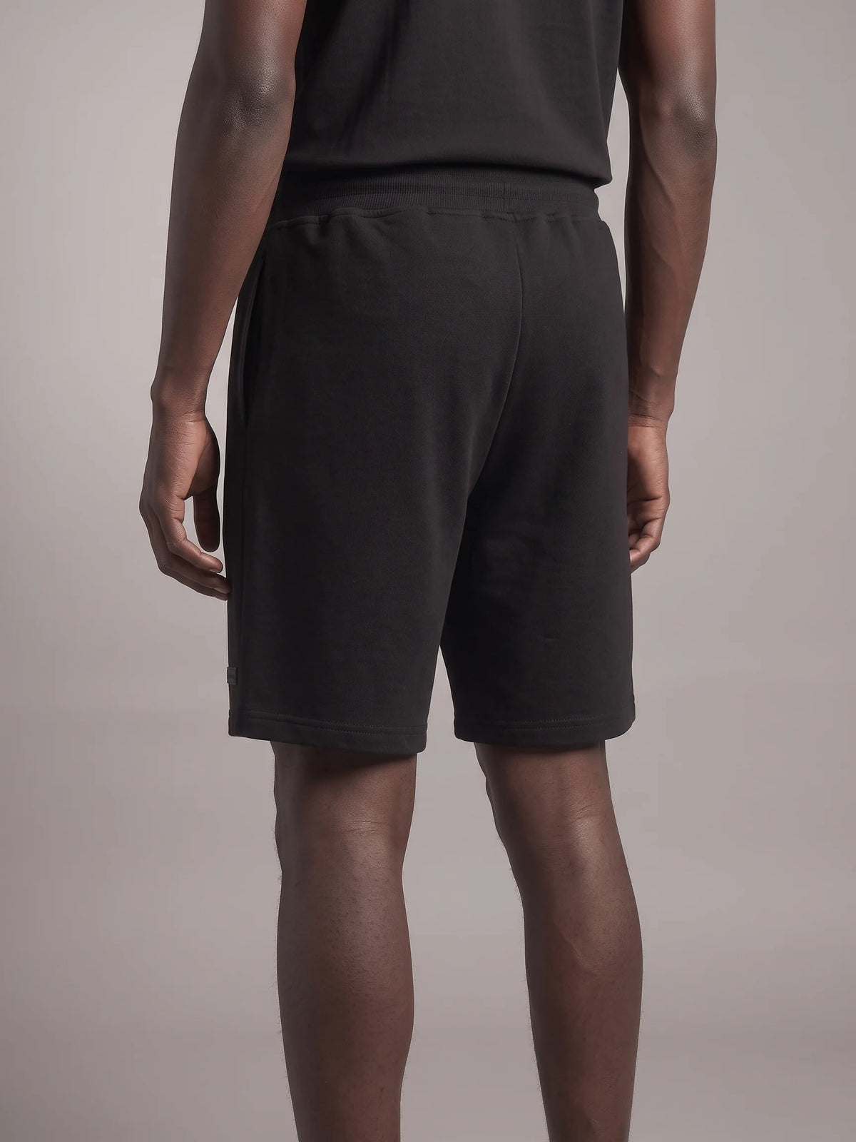 Black heavyweight sweat shorts in organic cotton, Unidentity Core Shorts, back view worn by man showing the relaxed fit, UAE streetwear #color_black
