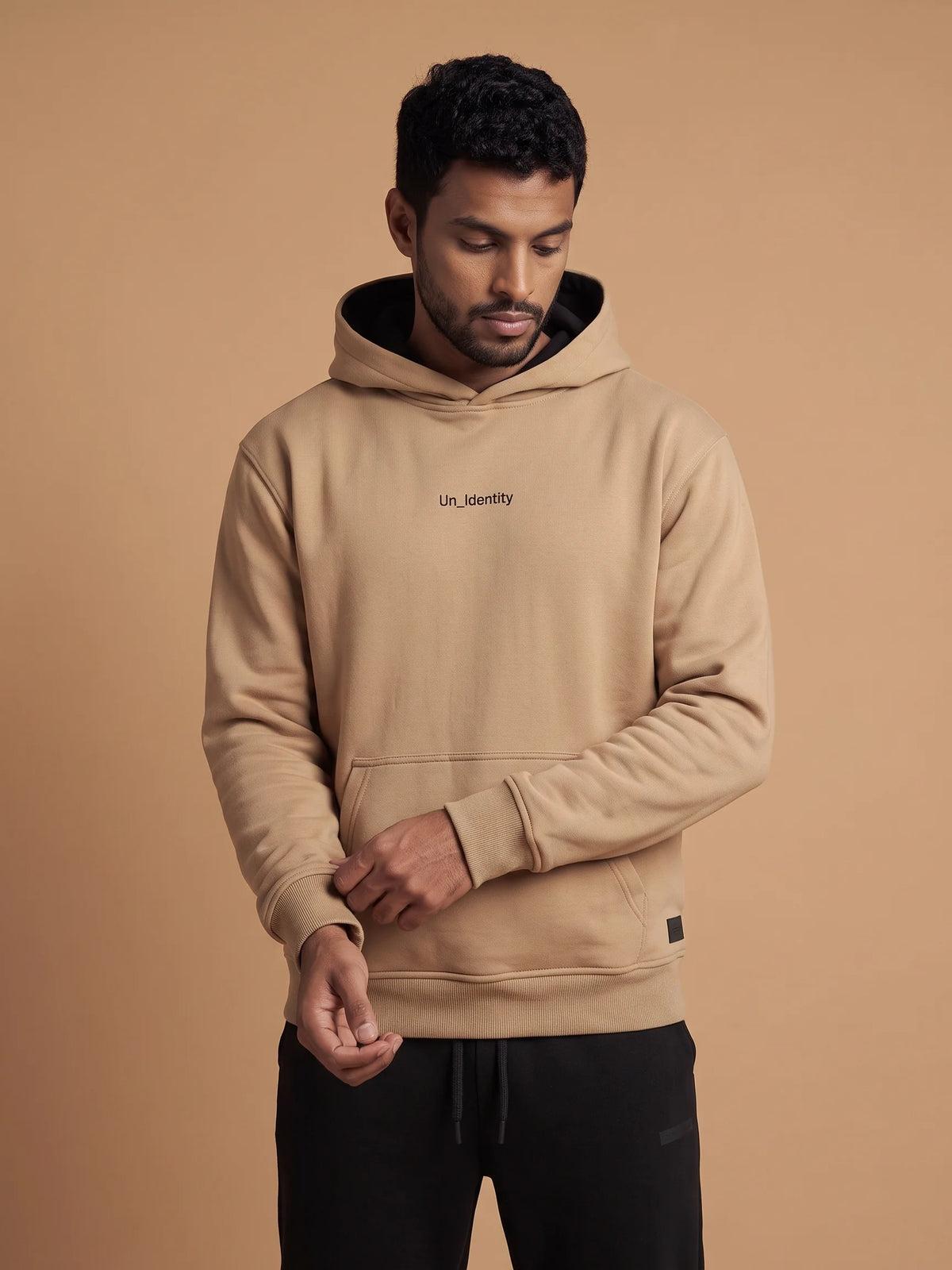 Beige heavyweight hoodie, Unidentity Soul Regular Fit Hoodie, front view of the chest logo and kangaroo pocket worn by man, streetwear brand in Dubai #color_beige