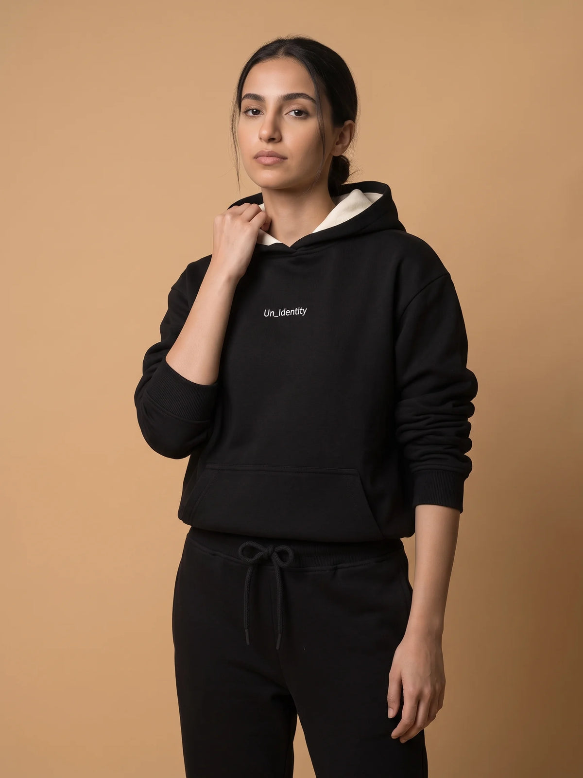 Black heavyweight hoodie, Unidentity Soul Hoodie, front view of the chest logo worn by woman with black Core joggers, streetwear brand in Dubai #color_black