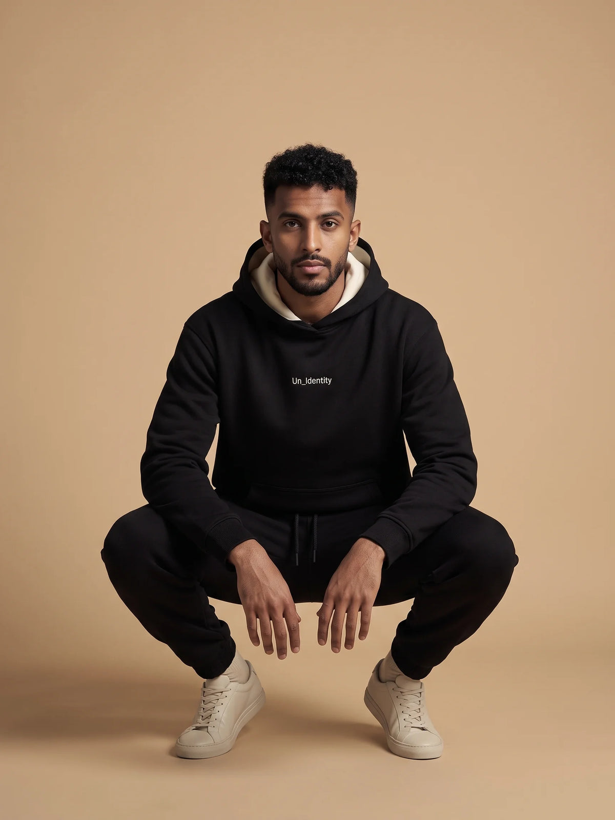 Black regular fit hoodie, Unidentity Soul Hoodie, front view of the heavyweight fit worn by man crouching with black Core joggers, sustainable fashion #color_black