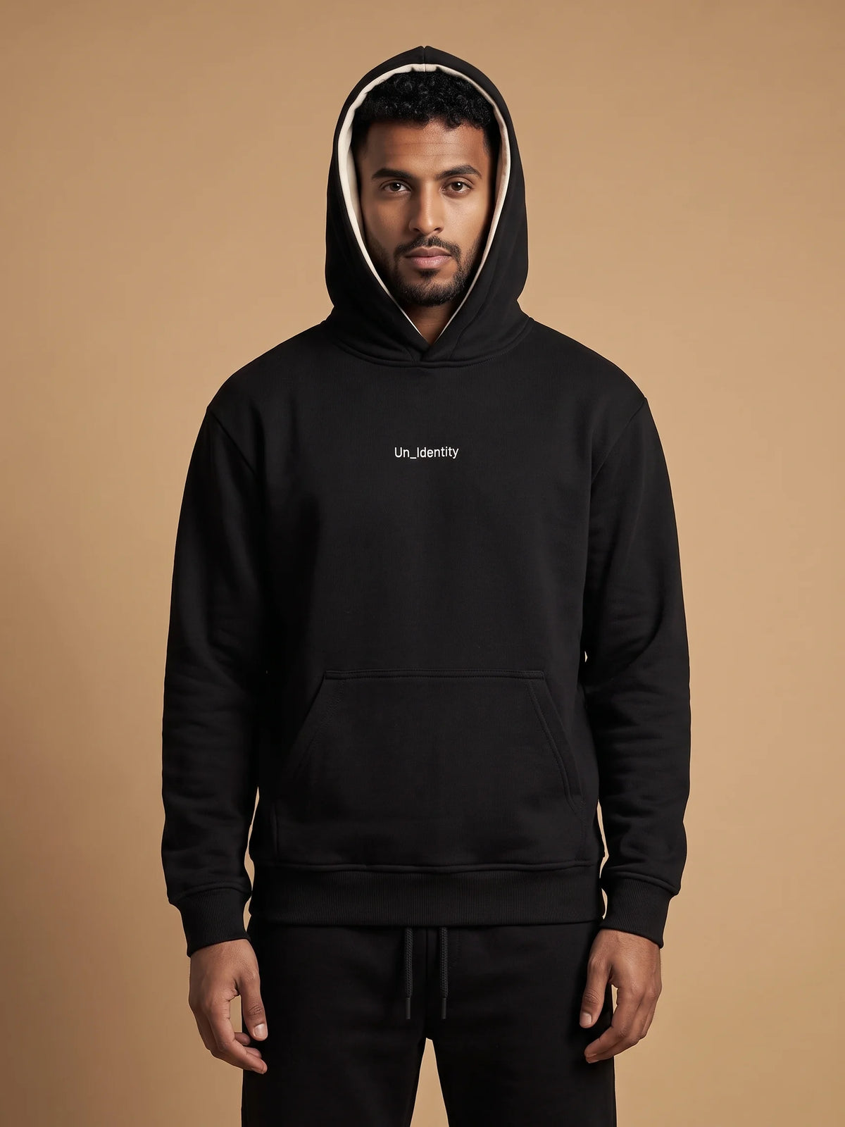 Black organic cotton hoodie, Unidentity Soul Hoodie, front view of the chest logo and contrast hood lining worn by man with hood up, streetwear #color_black