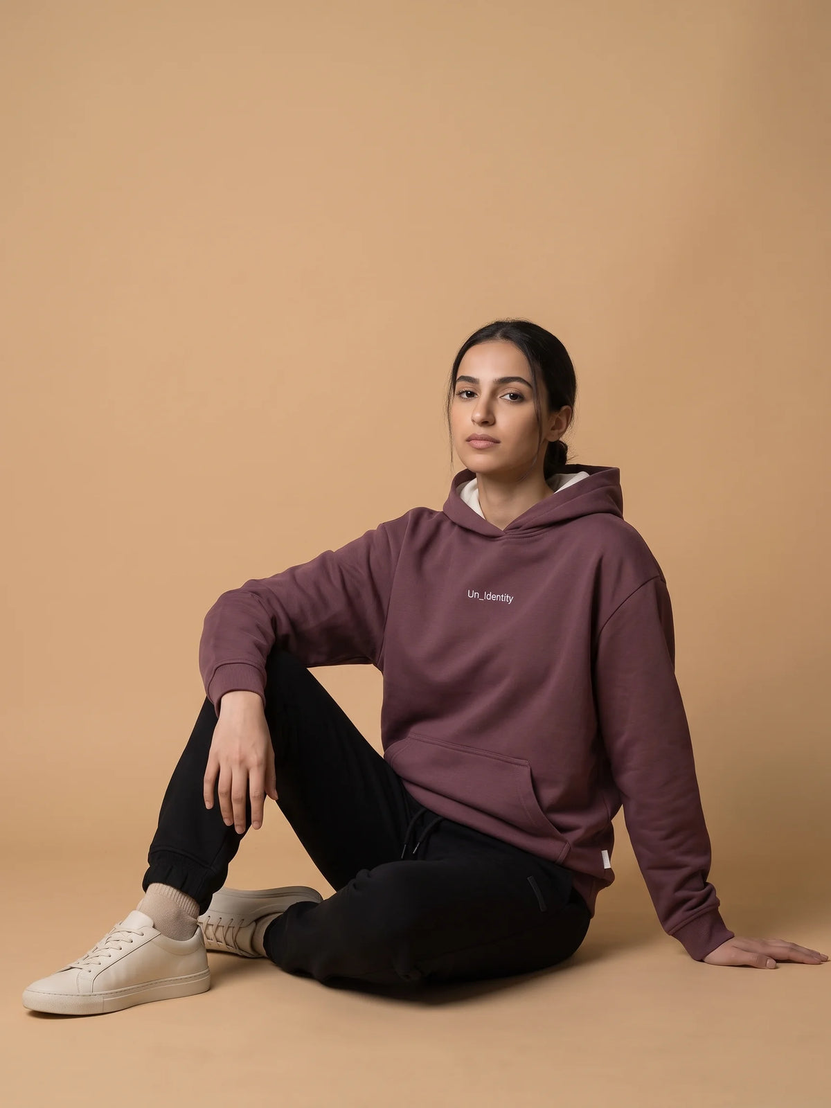 Plum heavyweight hoodie in organic cotton, Unidentity Soul Hoodie, front view worn by woman seated on the floor with black Core joggers, streetwear #color_plum