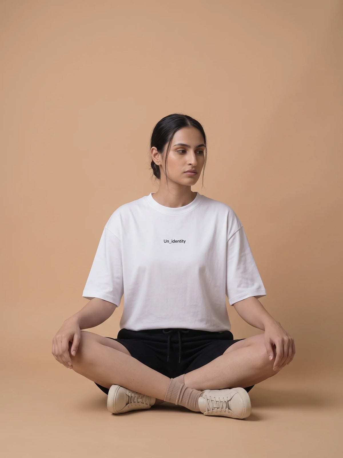 White oversized t-shirt, Unidentity Soul Oversized Tee, front view worn by woman seated cross-legged with black Core shorts, streetwear brand in Dubai #color_white