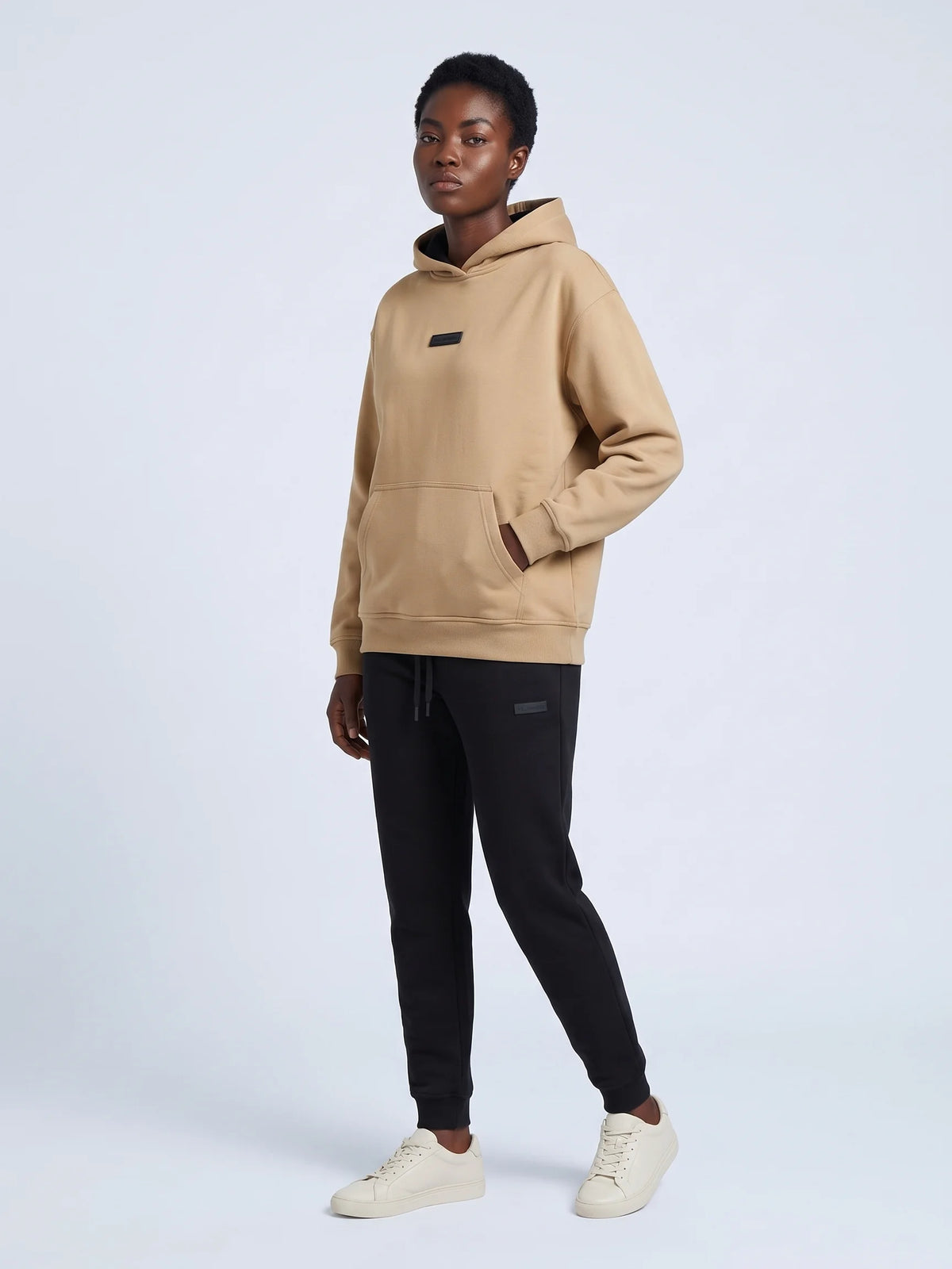 Beige organic cotton hoodie, Unidentity Identity Regular Fit Hoodie, full-length front view worn by woman, hand in kangaroo pocket, UAE streetwear #color_beige