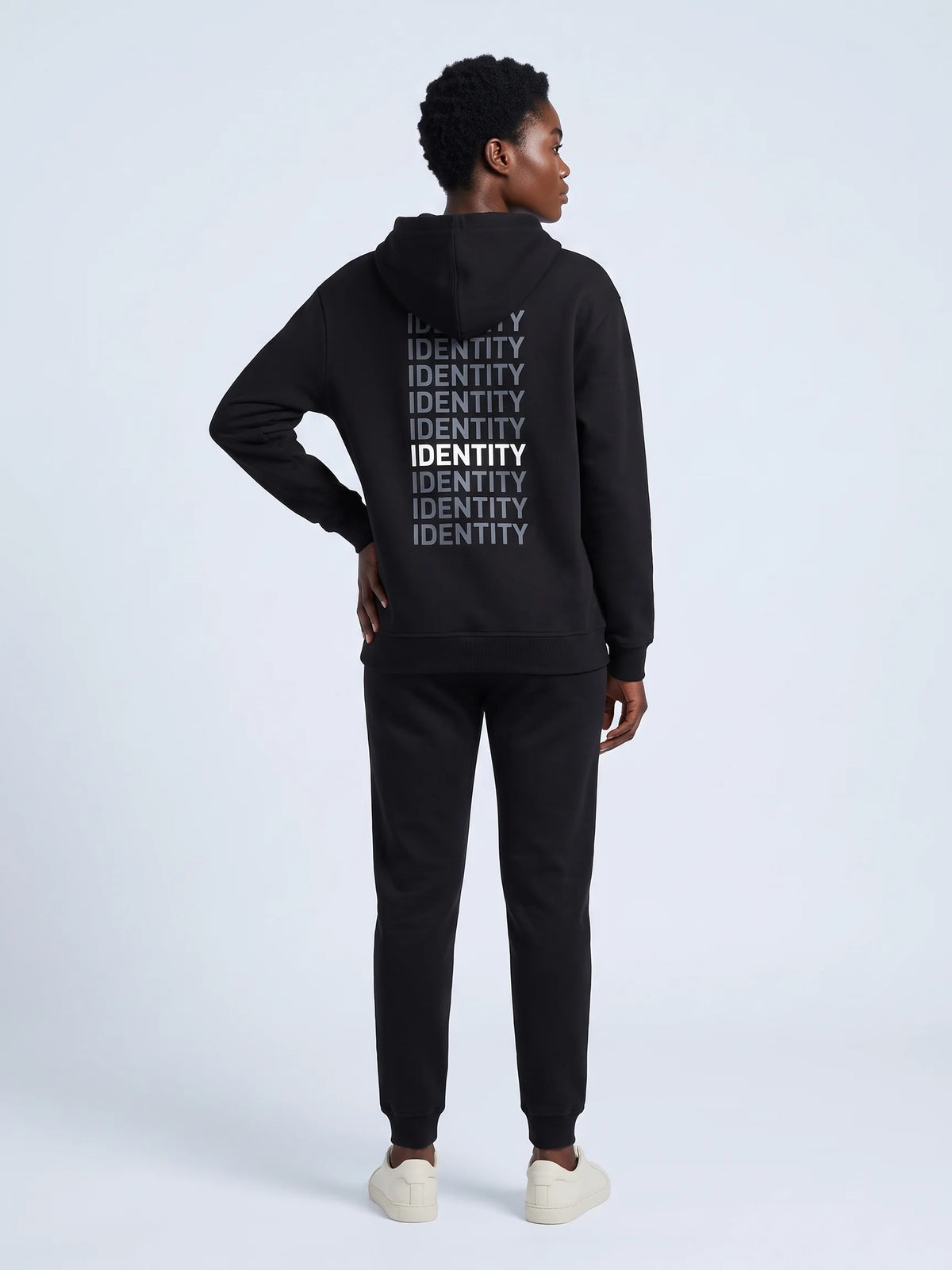 Black heavyweight hoodie in organic cotton, Unidentity Identity Hoodie, full-length back view of the IDENTITY print, hand on hip, UAE streetwear #color_black