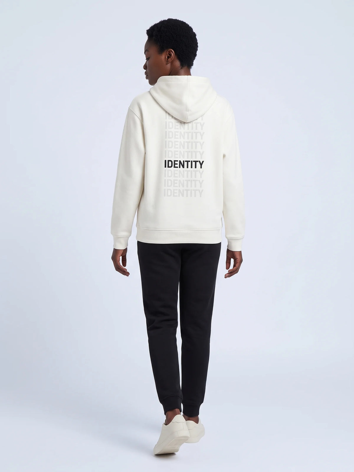 White regular fit hoodie in organic cotton, Unidentity Identity Hoodie, back view of the IDENTITY print worn by woman walking, sustainable fashion #color_white