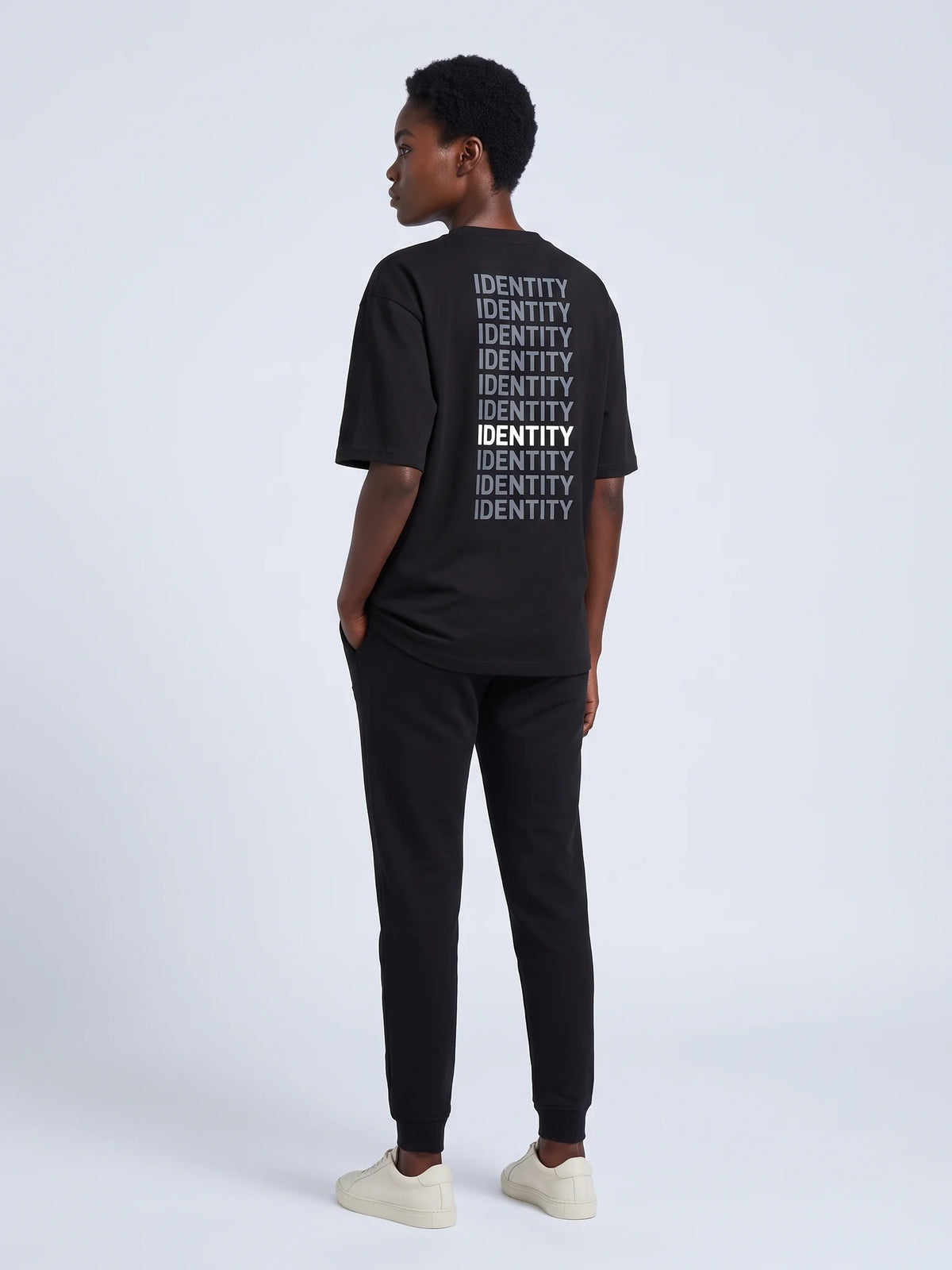Black heavyweight oversized t-shirt, Unidentity Identity Tee, three-quarter back view of the IDENTITY repeat print worn by woman, UAE streetwear #color_black